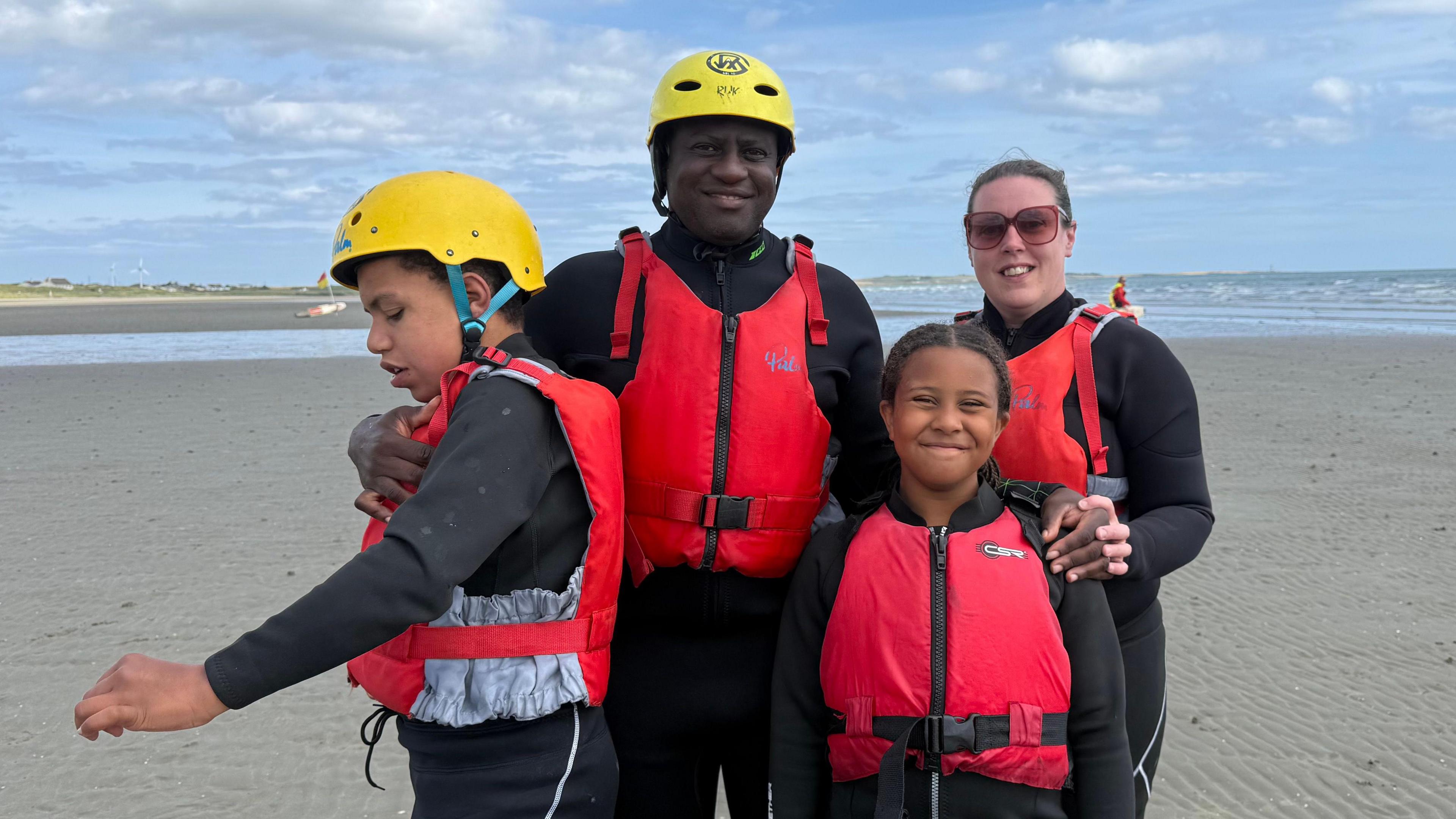 Family of four with black wetsuits and red life jackets.