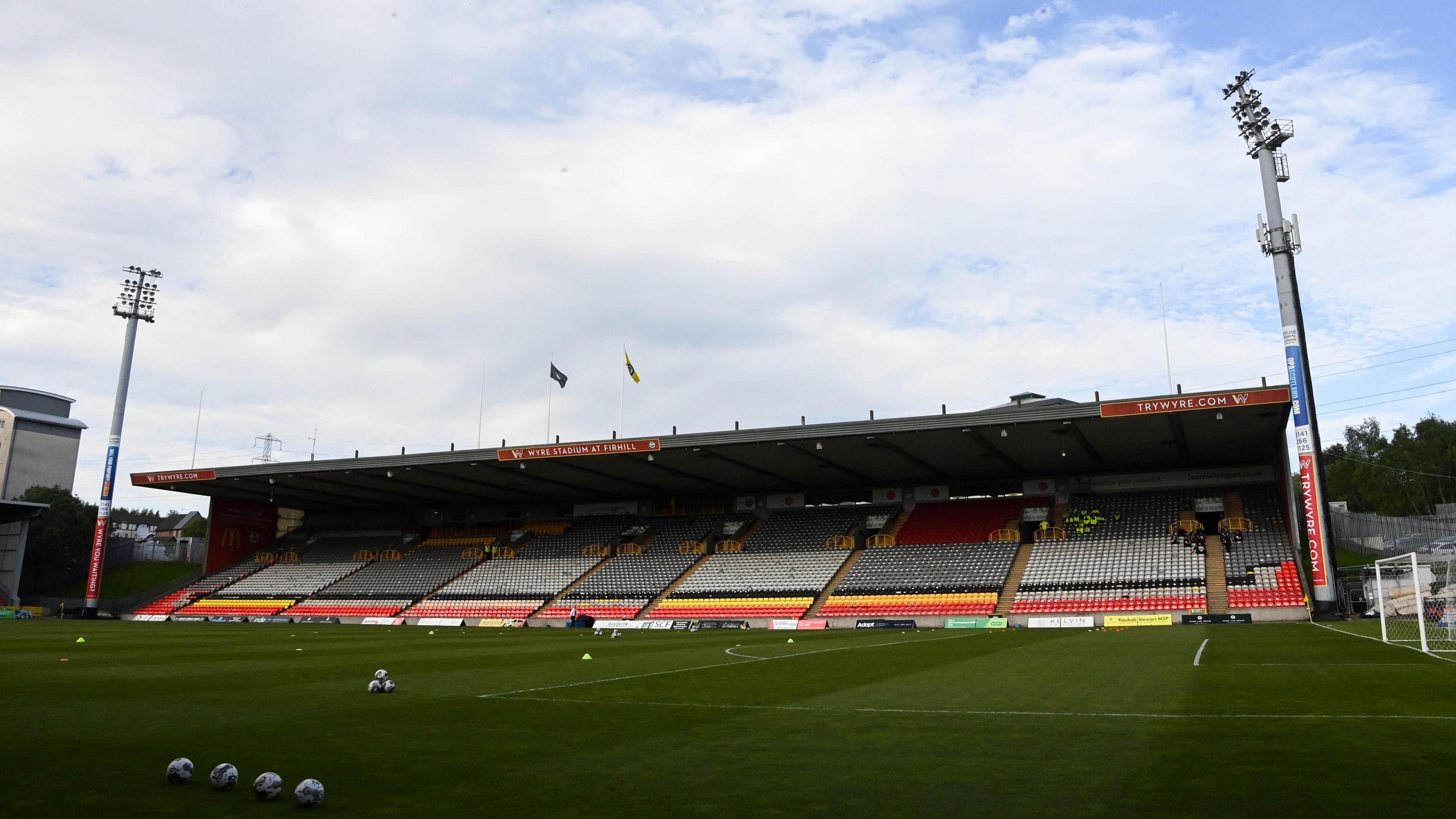 Empty Firrhill Stadium stand with floodlights at the side and balls on the pitch 