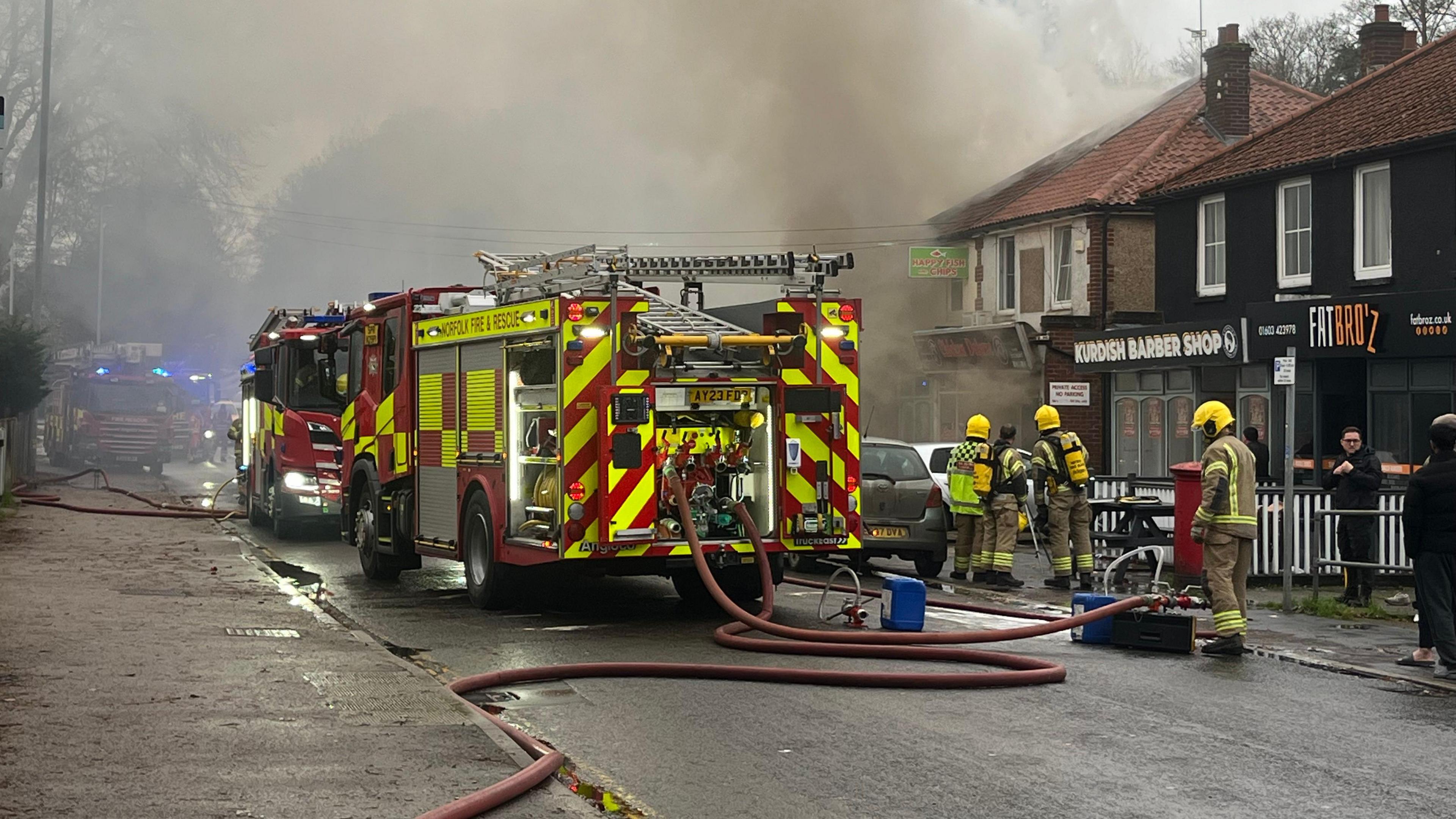 The scene of a fire in Norwich. Three fire engines and firefighters can be seen while smoke billows from a building in the background.