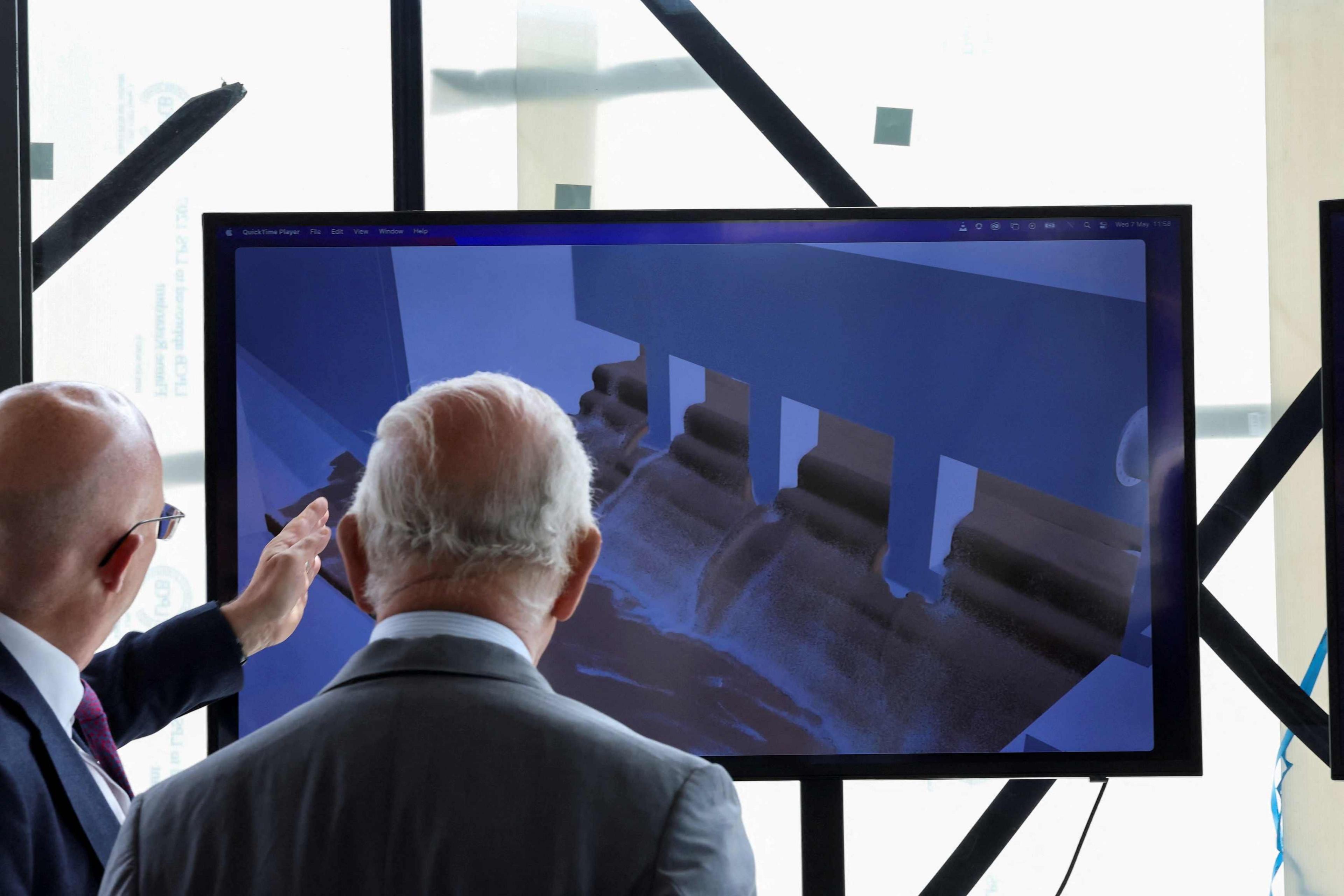 King Charles III watches a video demonstration a on screen during a visit