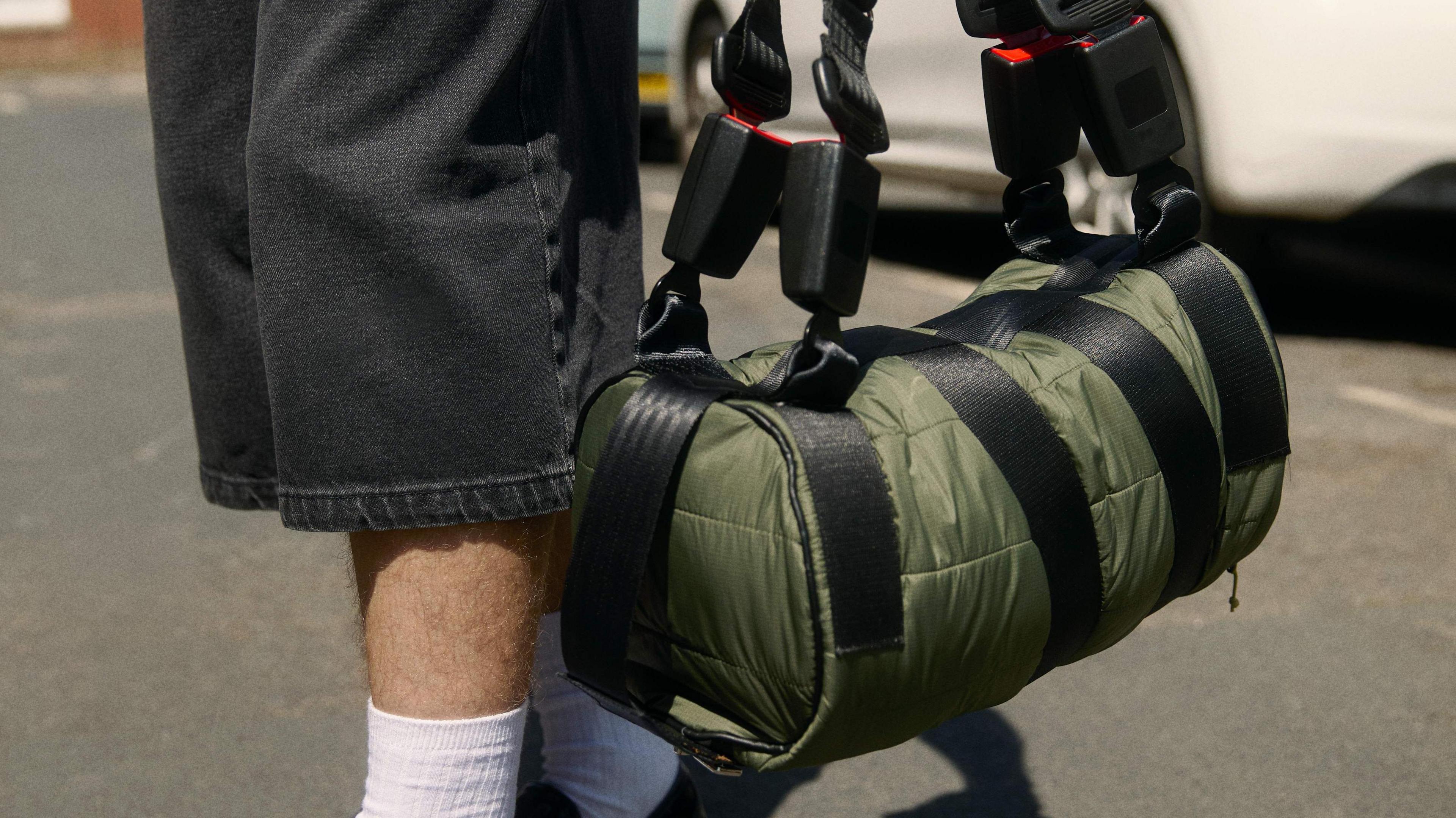 A closeup of a green duffel bag with seat belts and buckles making up the straps.