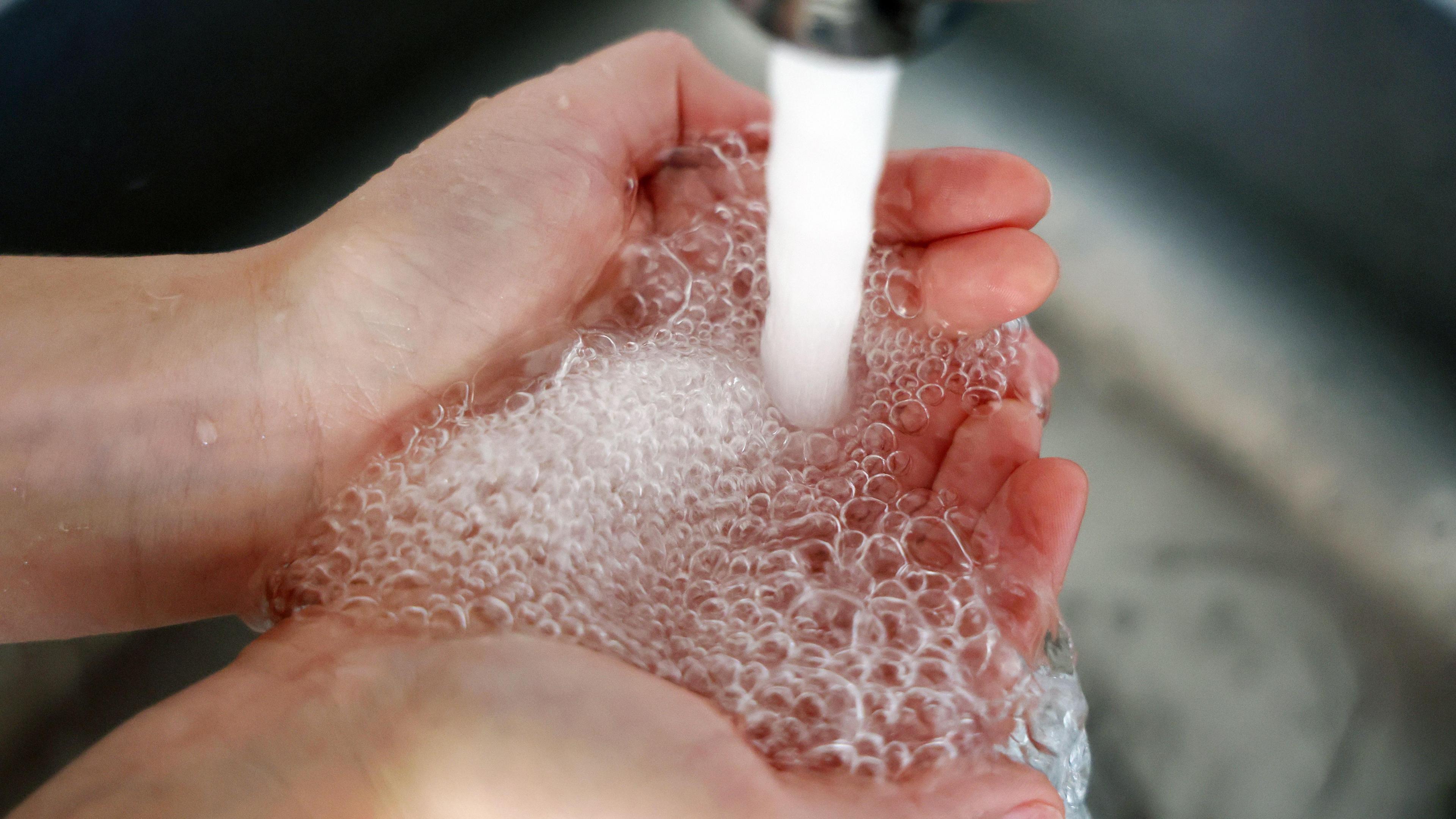 Water runs through a persons hands into a metal sink from a tap at a home. 