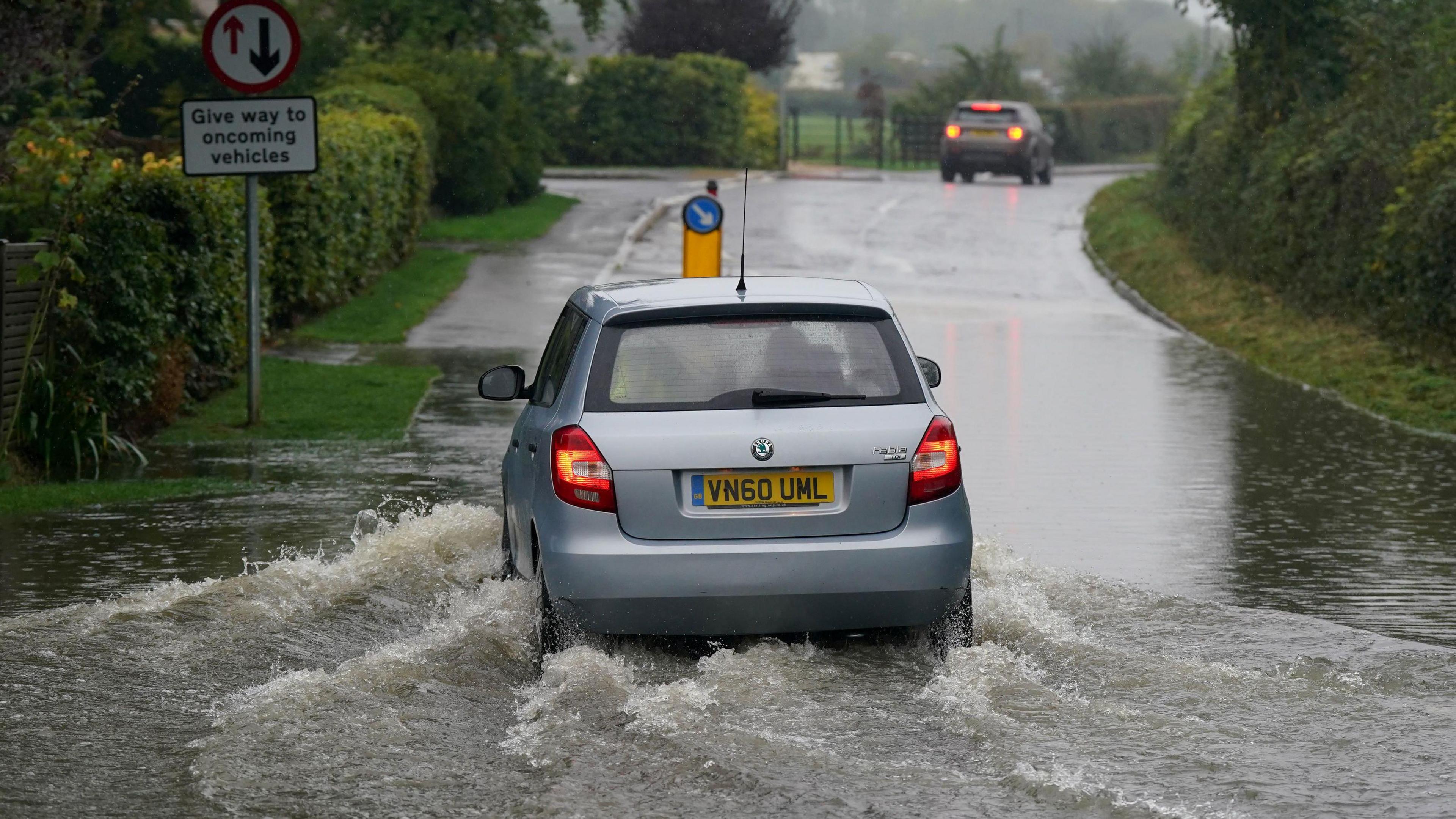 A silver car drives through a flooded road in Willersey village, Gloucestershire. 