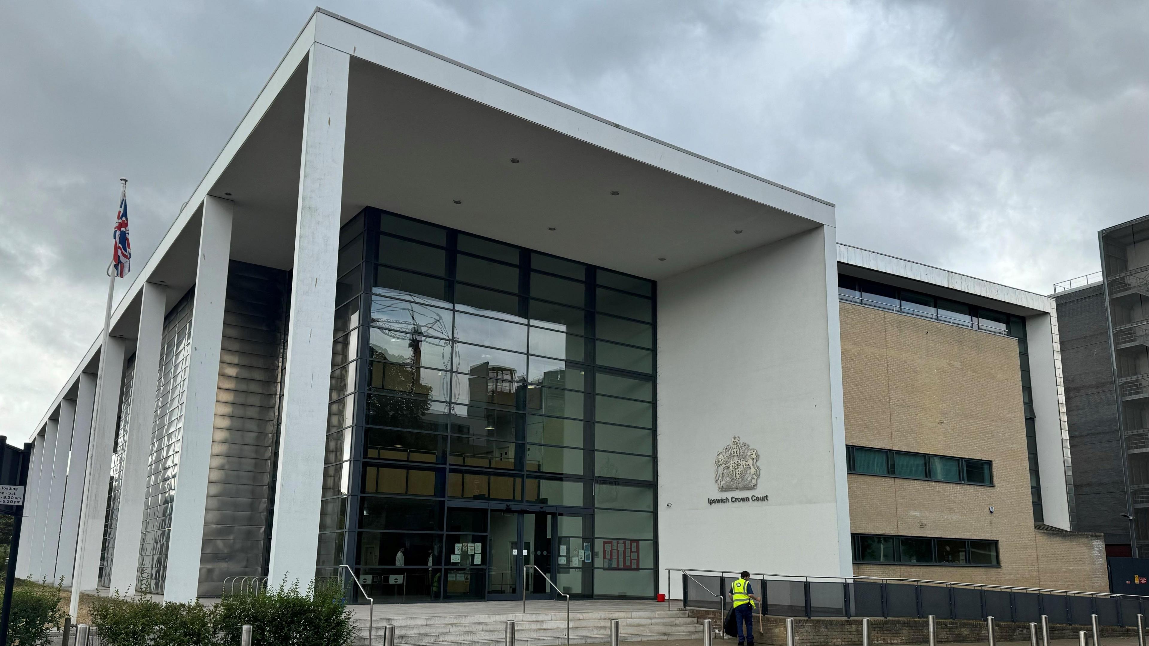 The frontage of Ipswich Crown Court, in Ipswich. The front of the building is predominately glass with a white concrete border, on which the Ipswich Crown Court crest is displayed.