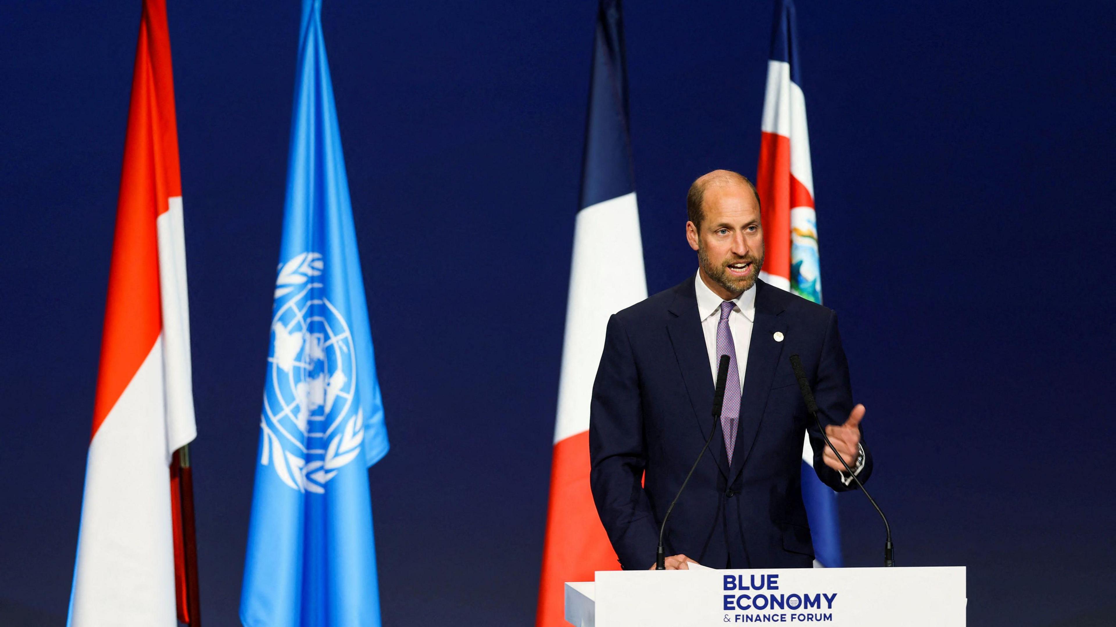 prince william at a podium in front of flags