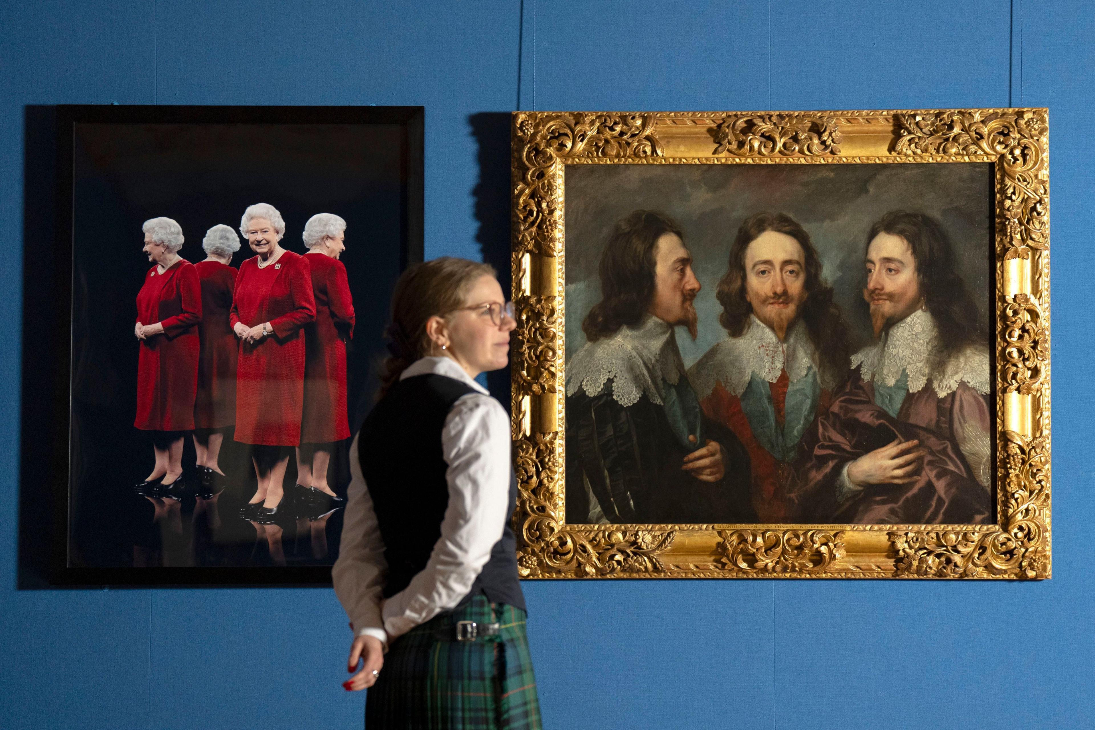 A curator wearing a kilt and white shirt with black wasitcoat stands next two two paintings - one of the Queen in a red dress and the other of Charles I with long brown hair and pointy beard.