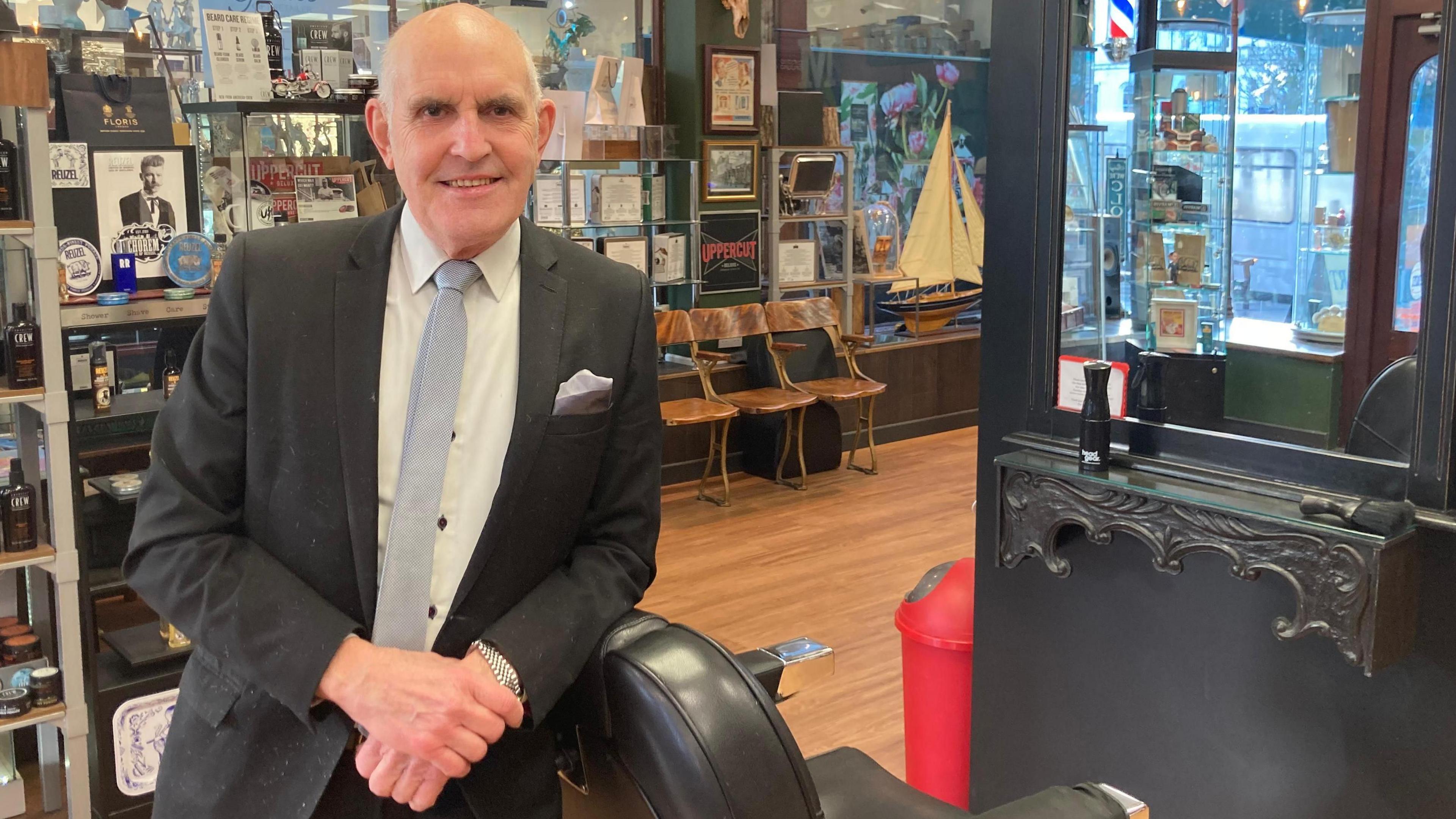 Rob Rix in charcoal grey suit, white shirt and light grey tie by his barber's chair