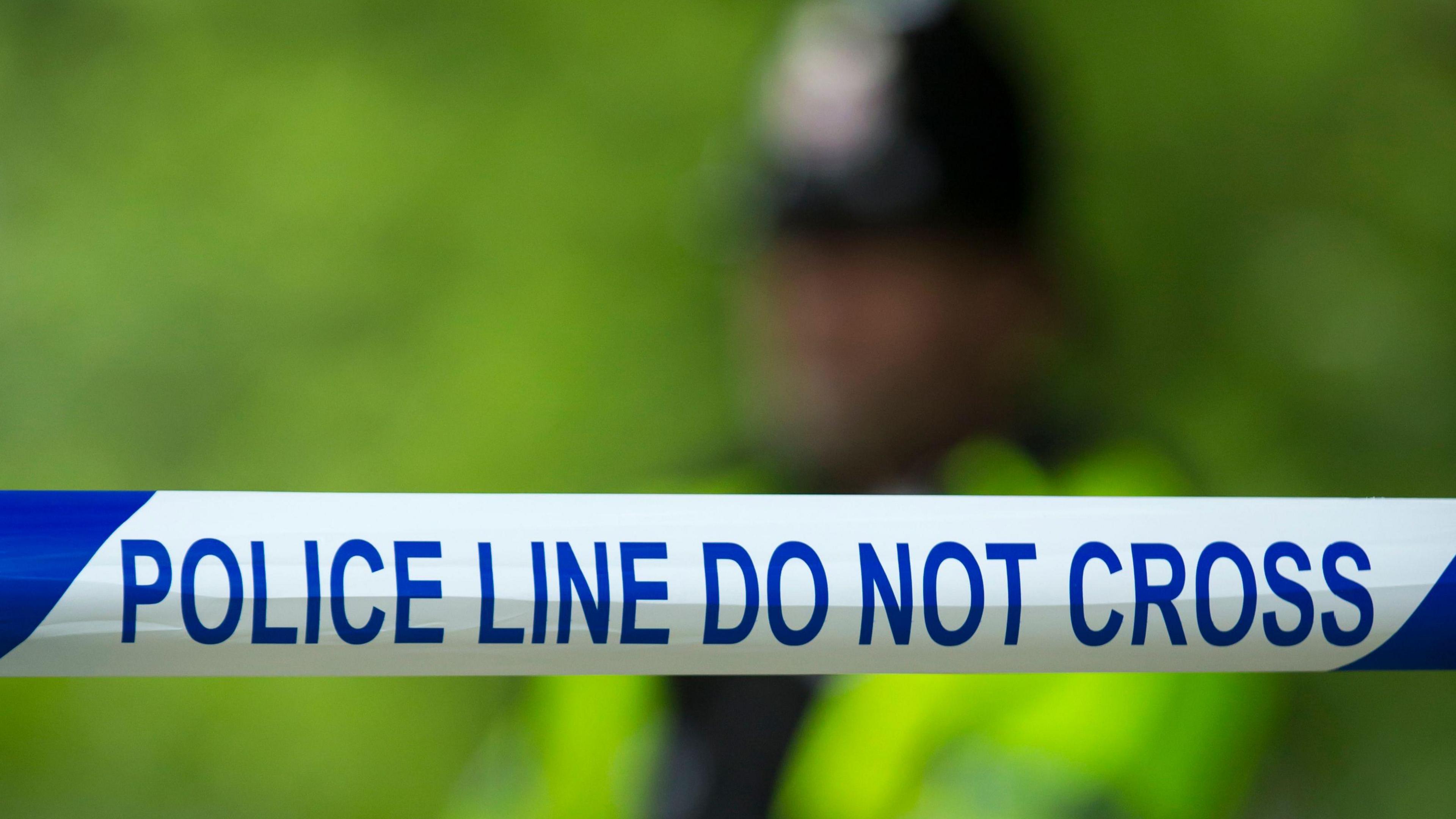 A general view of a police cordon, with the words 'police line do not cross', with an officer in high vis clothing, blurred out in the background