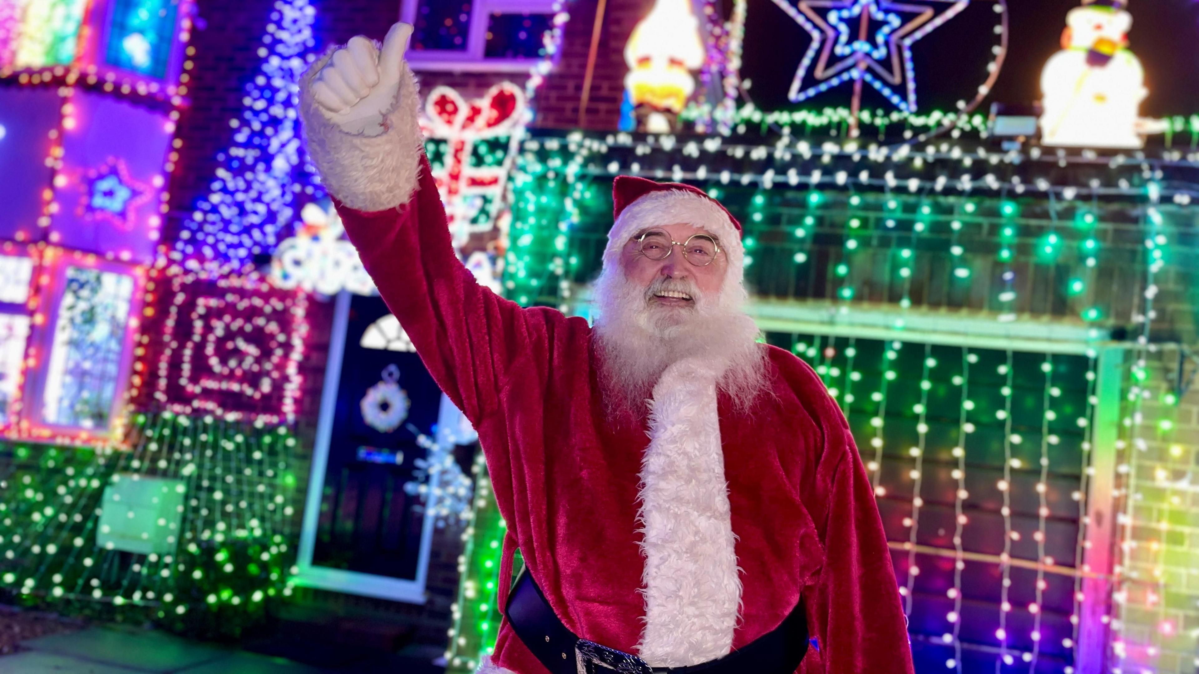 Anthony O'Toole dressed as Santa in front of his brightly-lit house which is covered in lights