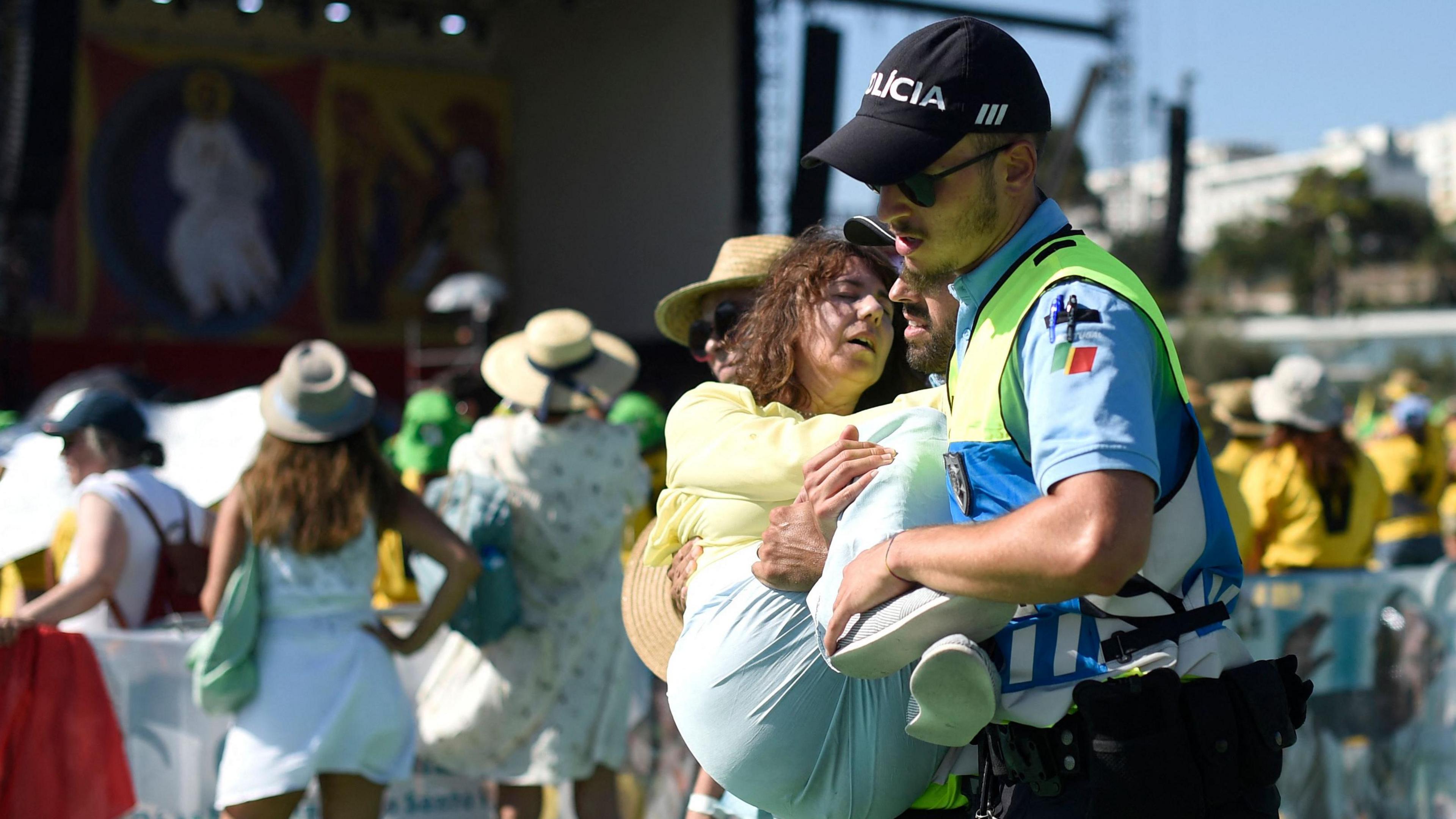 A woman is carried by a police officer after collapsing in high temperatures in Lisbon in 2023