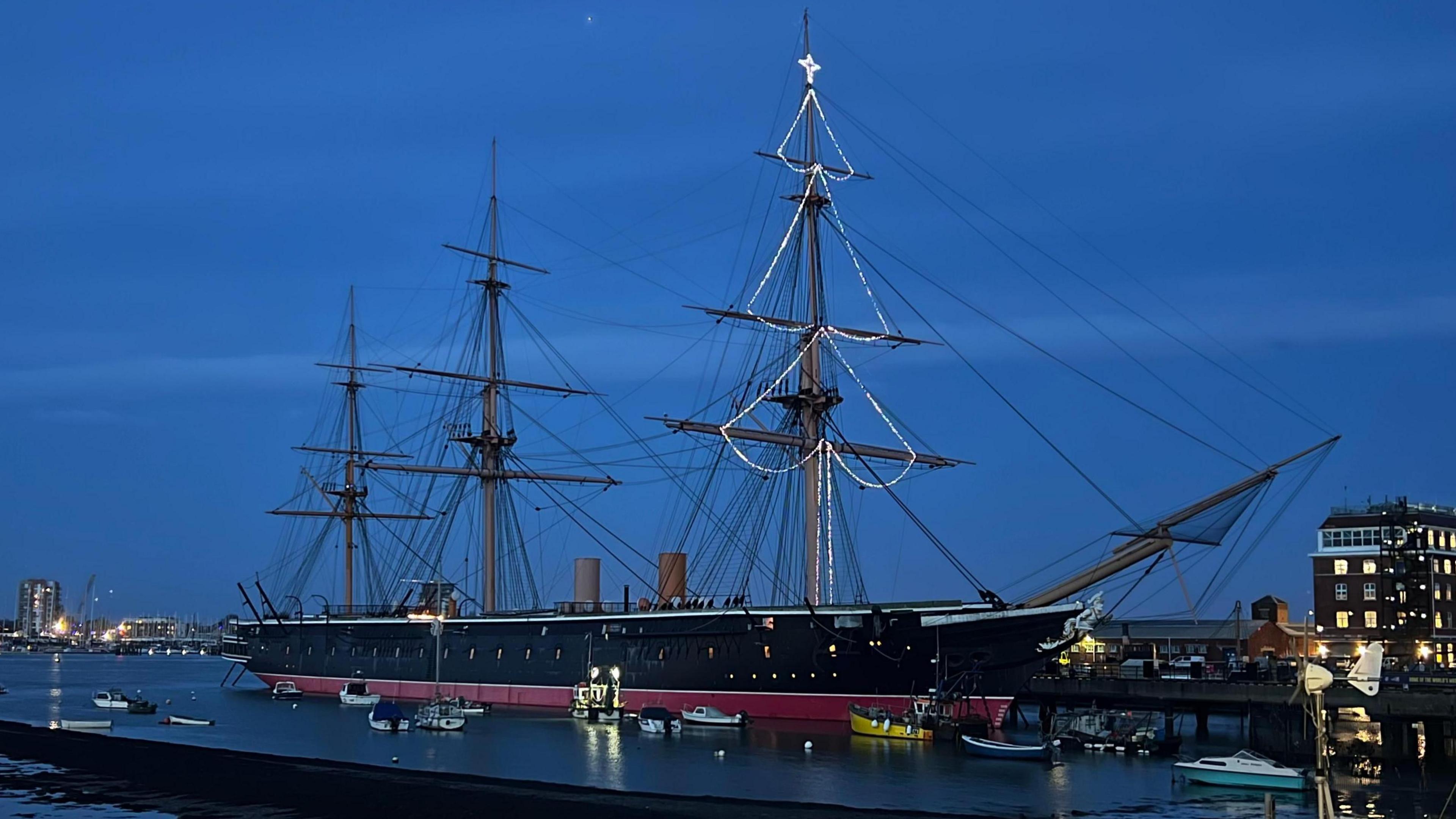 Iron-hulled warship, HMS Warrior, with christmas lights creating a tree shape in its mast.