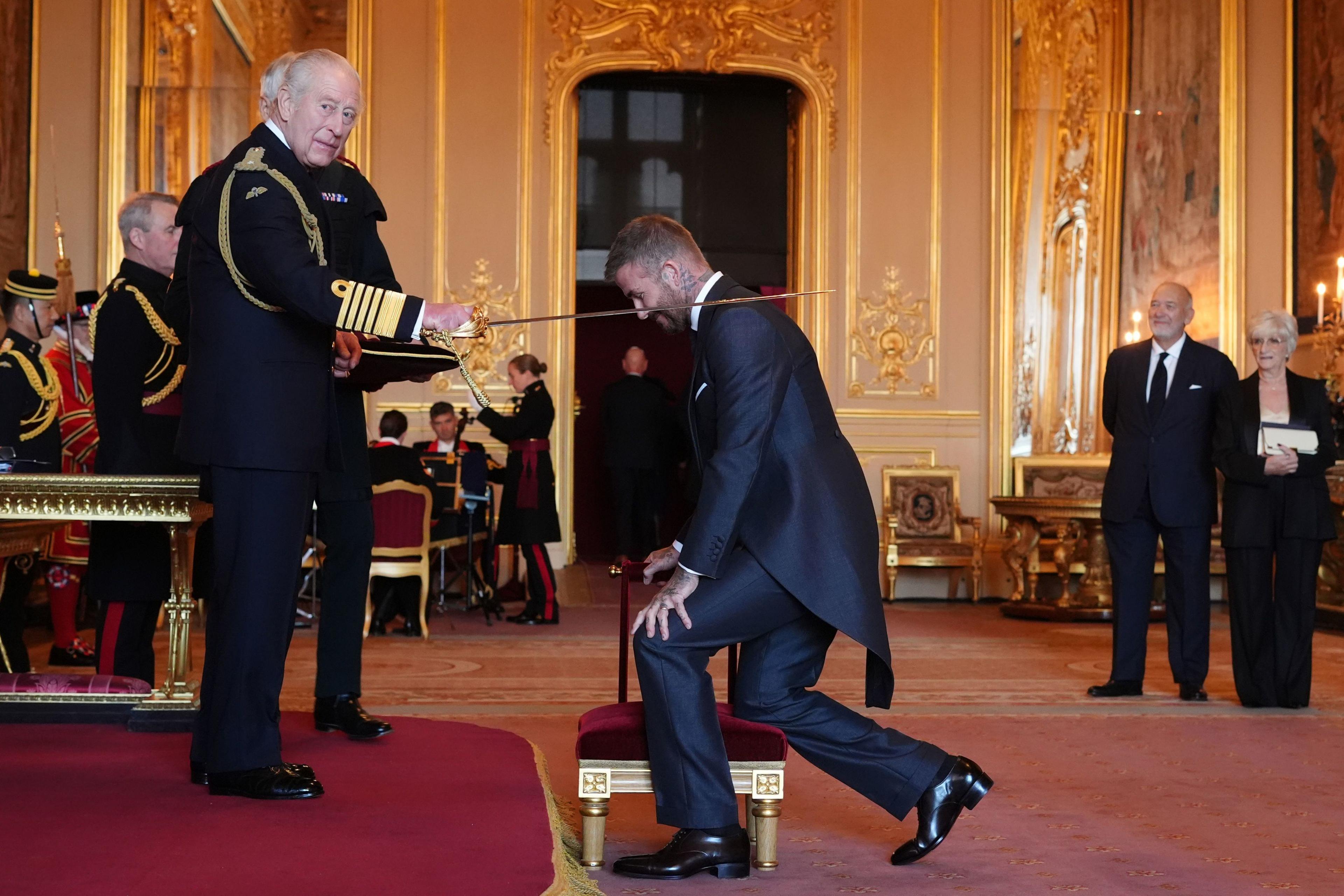 Sir David Beckham kneels as King Charles places a sword on his shoulder