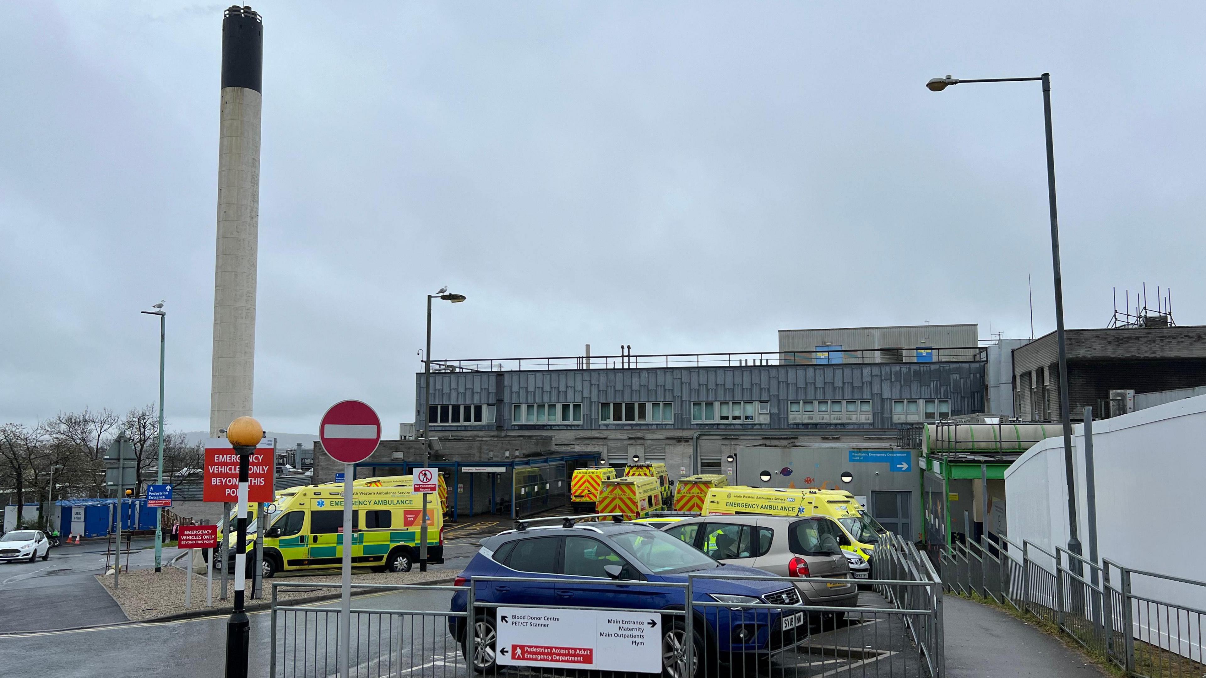 Exterior of Derriford Hospital. Ambulances and cars are parked outside.