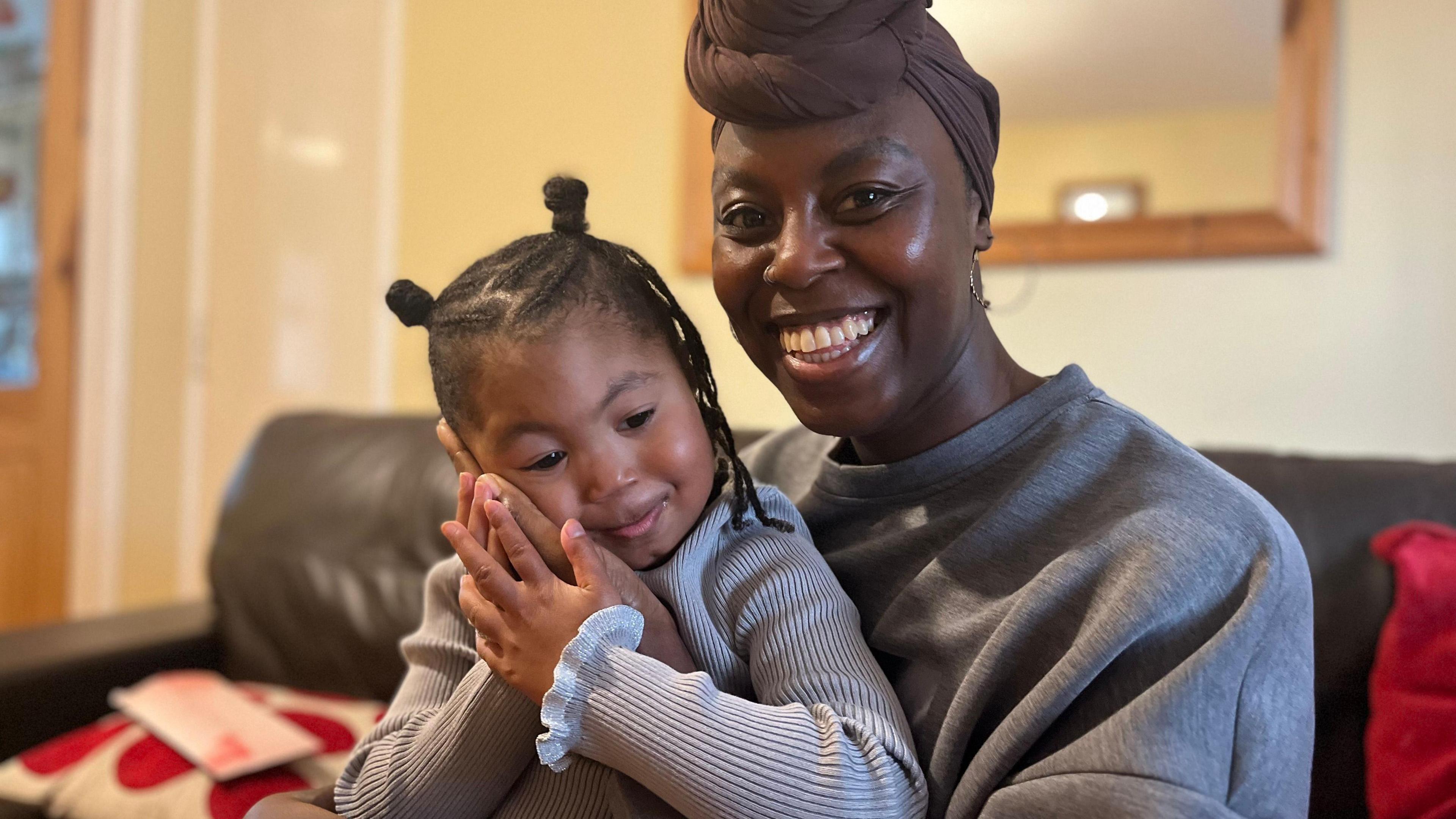 Dominique Belgrave, 31, from Woodhouse, sits on a sofa with her daughter Imaani, four, on her knee