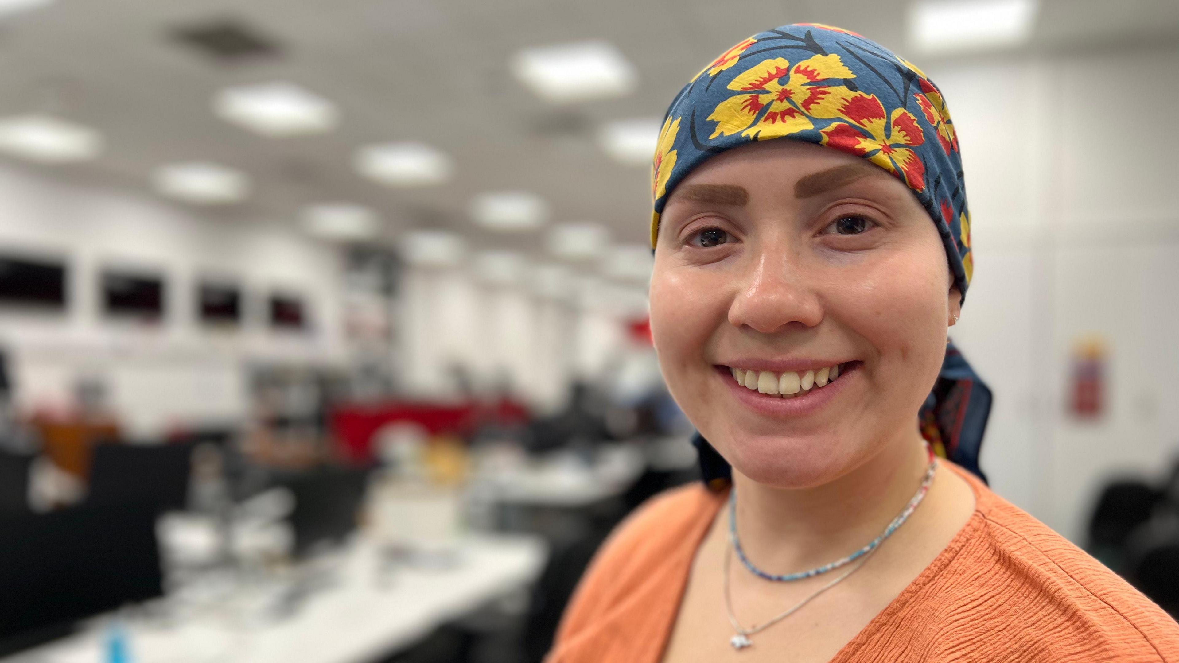 Dr Leanne Archer smiles at the camera. She wears a blue and yellow floral headscarf and a peach coloured top.