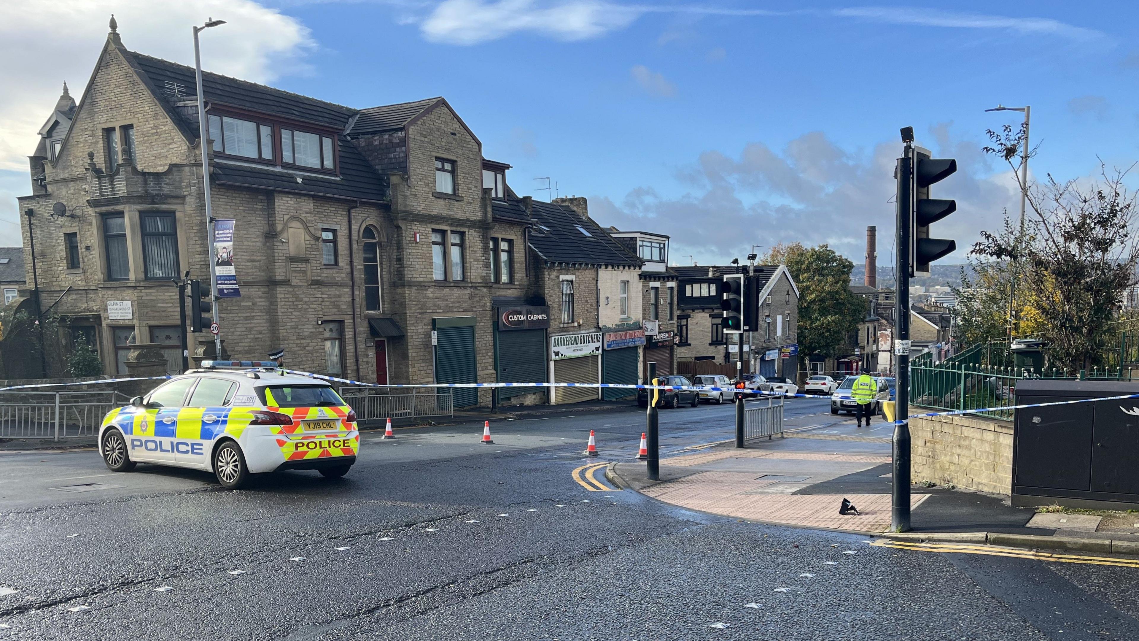 A police car is parked across the junction of a road that has been taped off with blue and white crime scene tape.