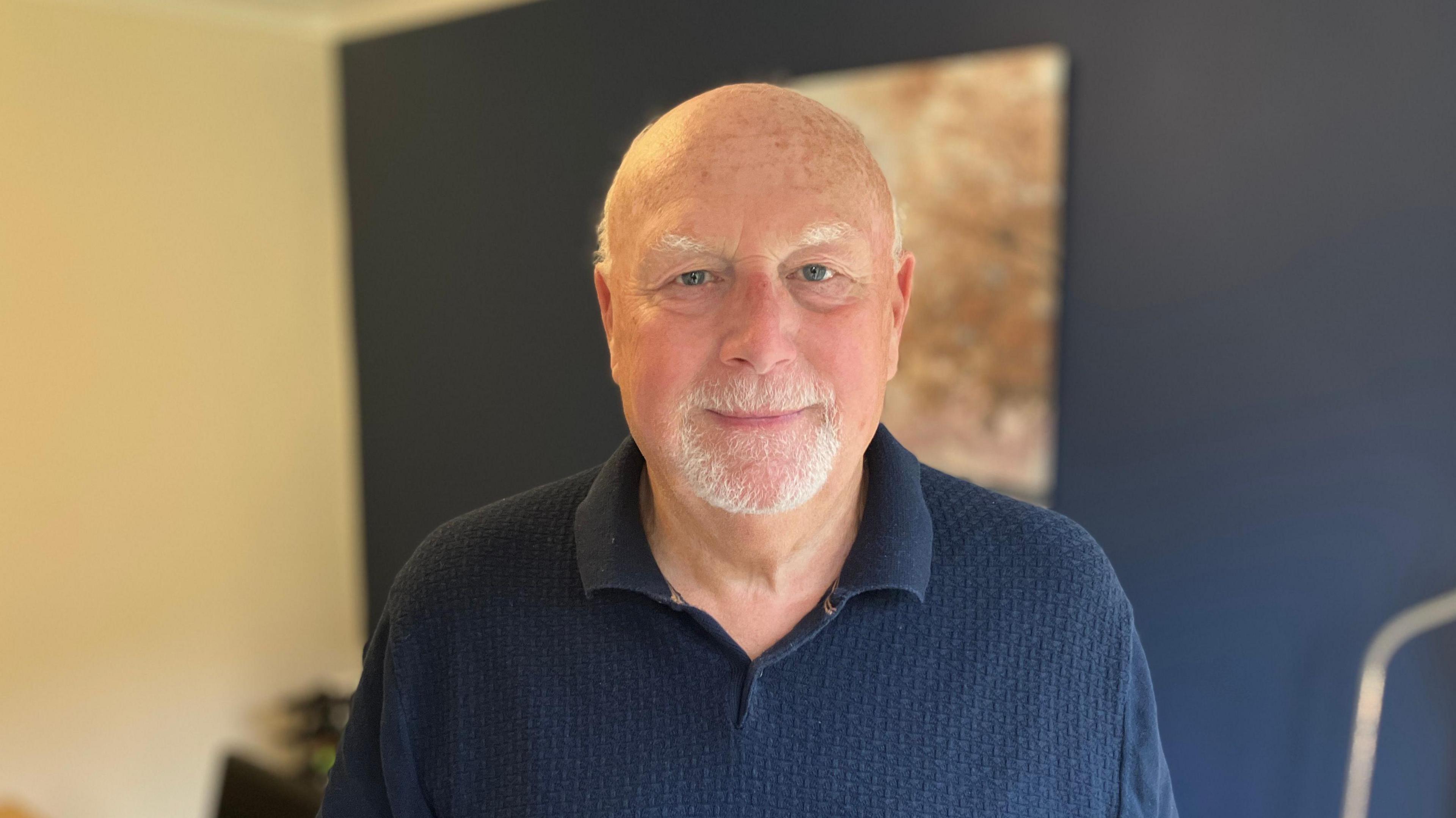 Michael Kinnear has short grey hair and beard. He is looking at the camera and wears a dark blue polo shirt