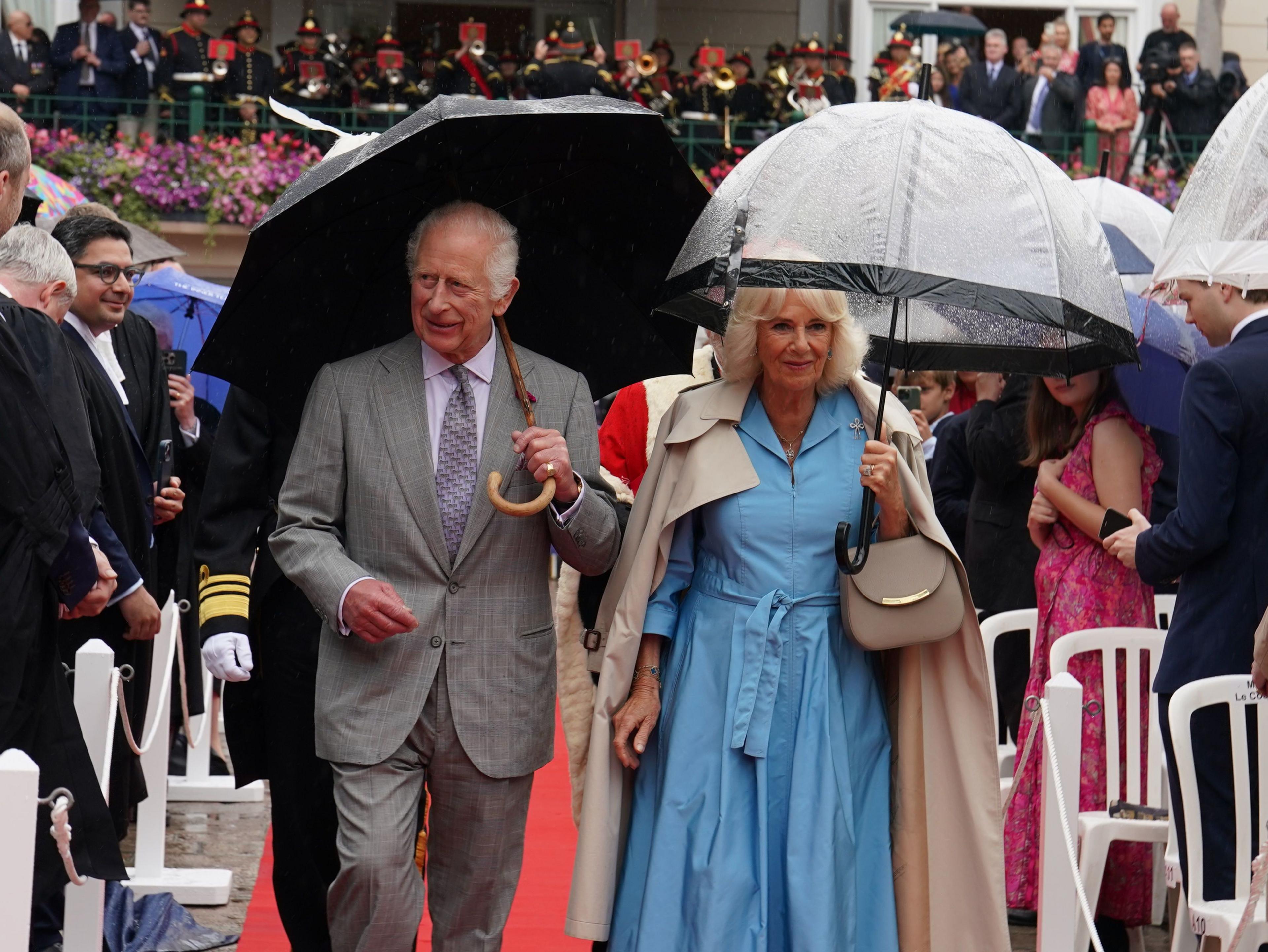 King Charles III and Queen Camilla carrying umbrellas and walking through Jersey's Royal Square