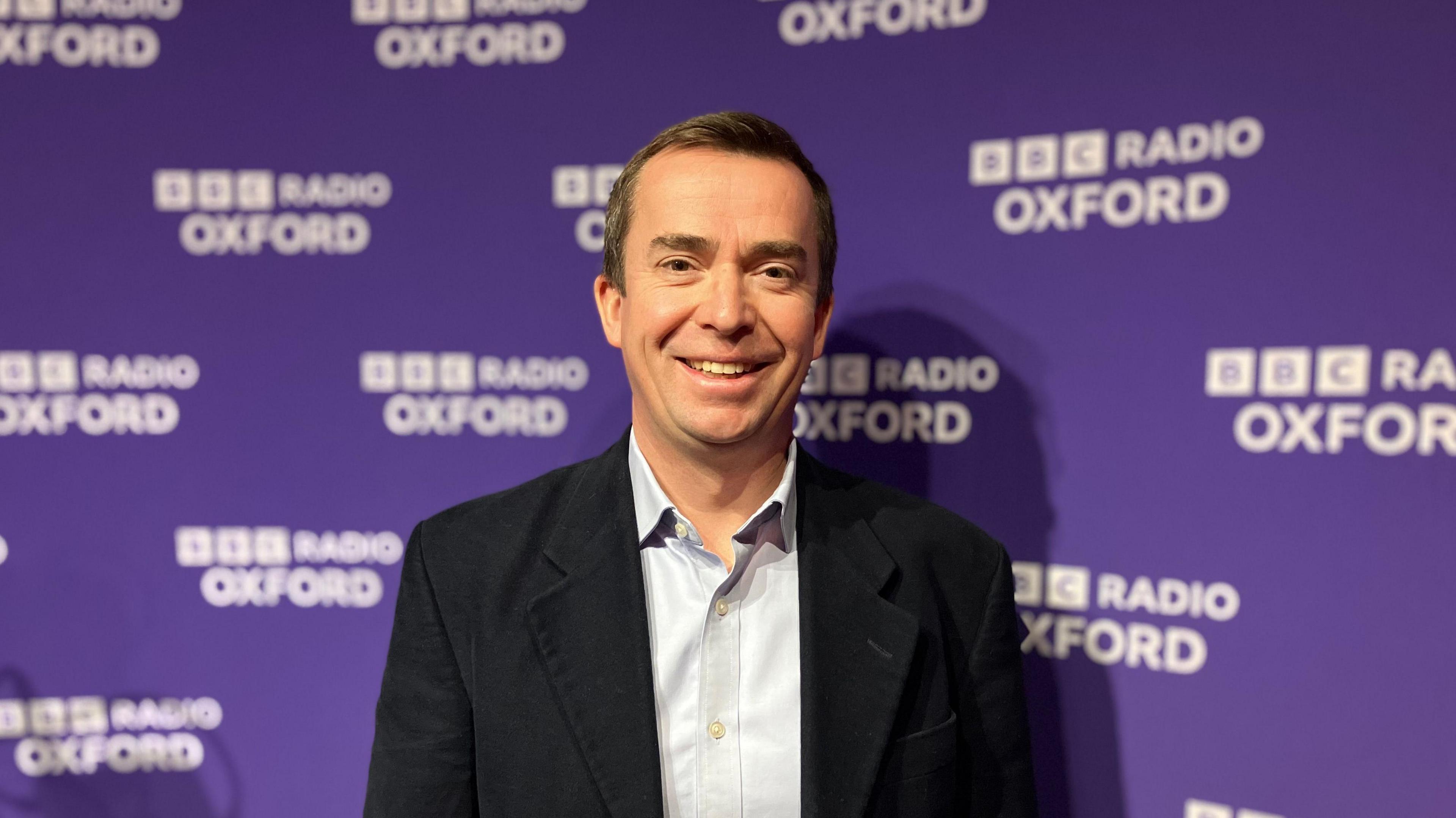 Calum Miller, the Liberal Democrat MP for Bicester & Woodstock, standing in front of a purple banner with "BBC Radio Oxford" branding. 