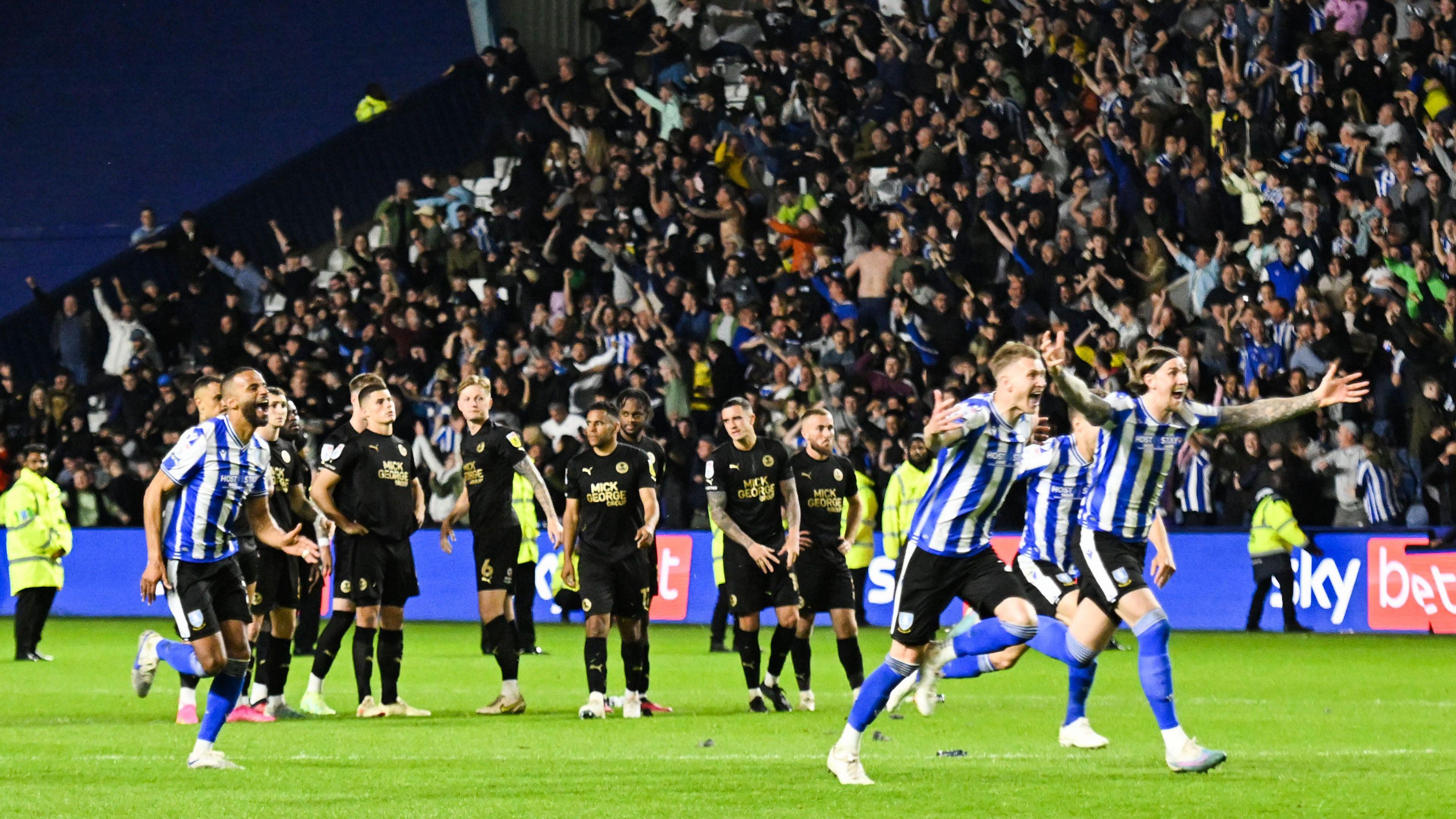 Sheffield Wednesday players in blue and white striped shirts begin the celebrations as they win the penalty shoot out and head for the play-off final as the Peterborough United players in black kits look dejected