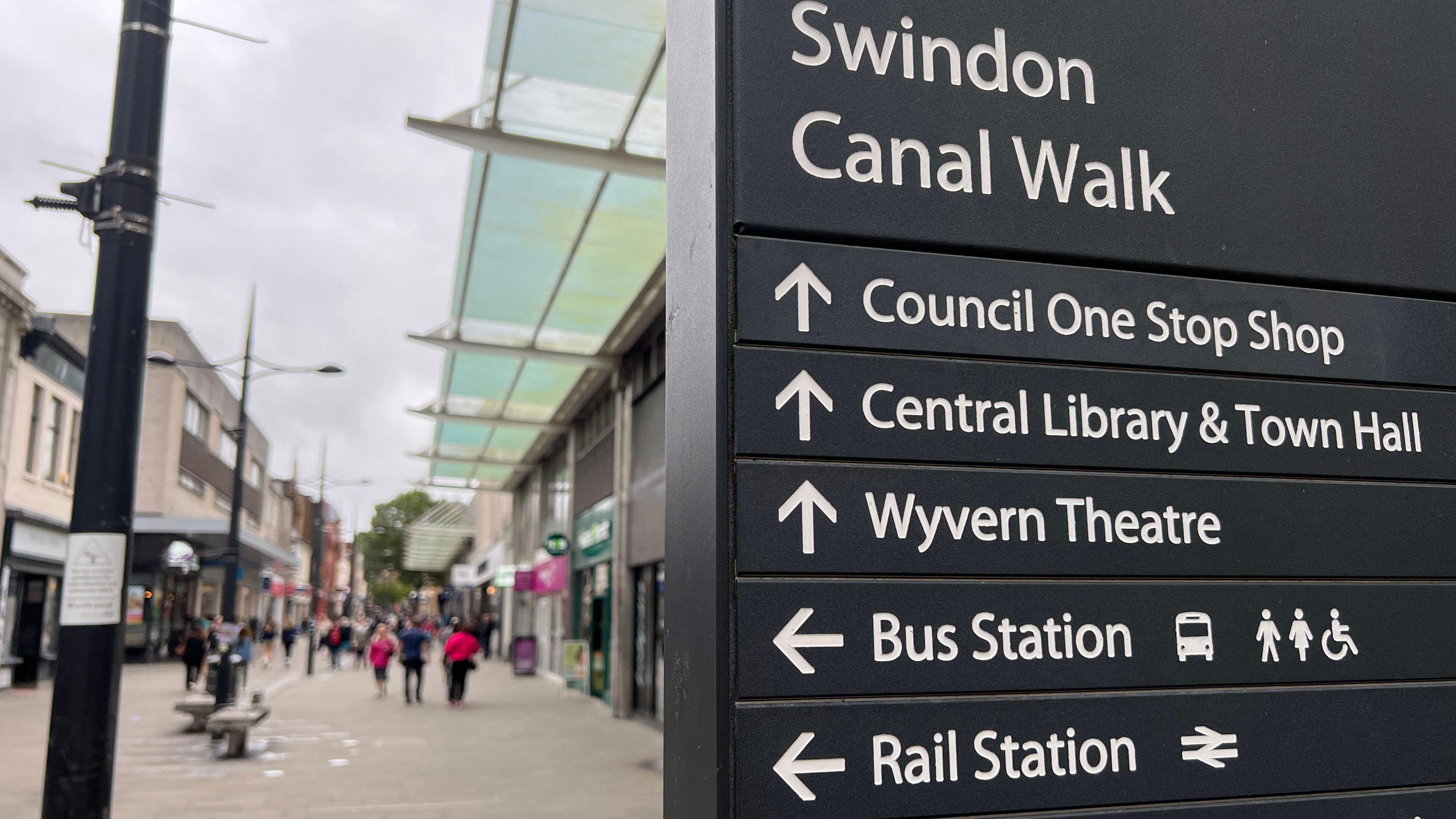 A sign in Swindon town centre showing the road name of Canal Walk, and a sign post pointing to various locations including the bus and railway stations and the Wyvern Theatre