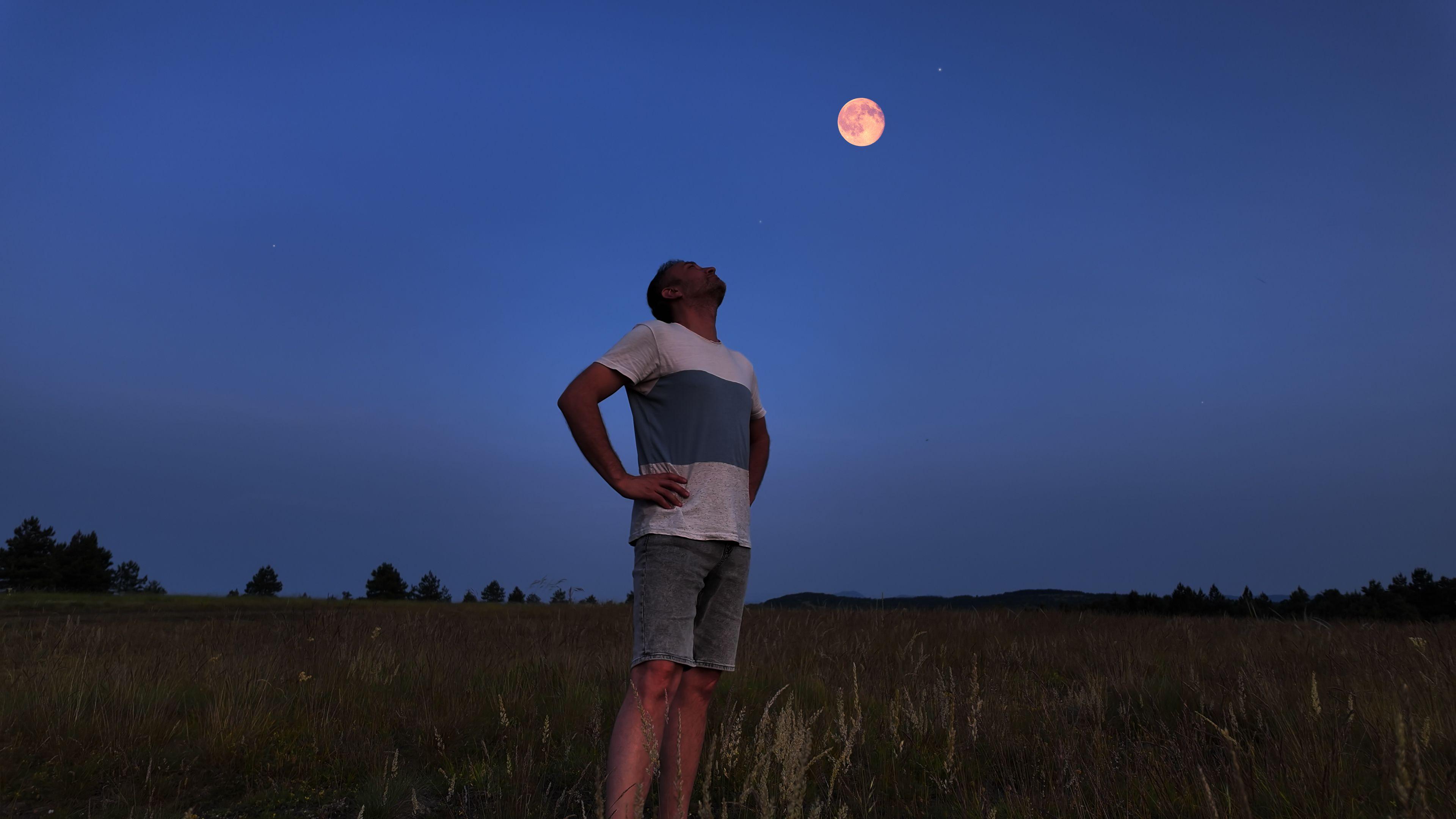 Amateur astronomer standing in a field looking up at the moon