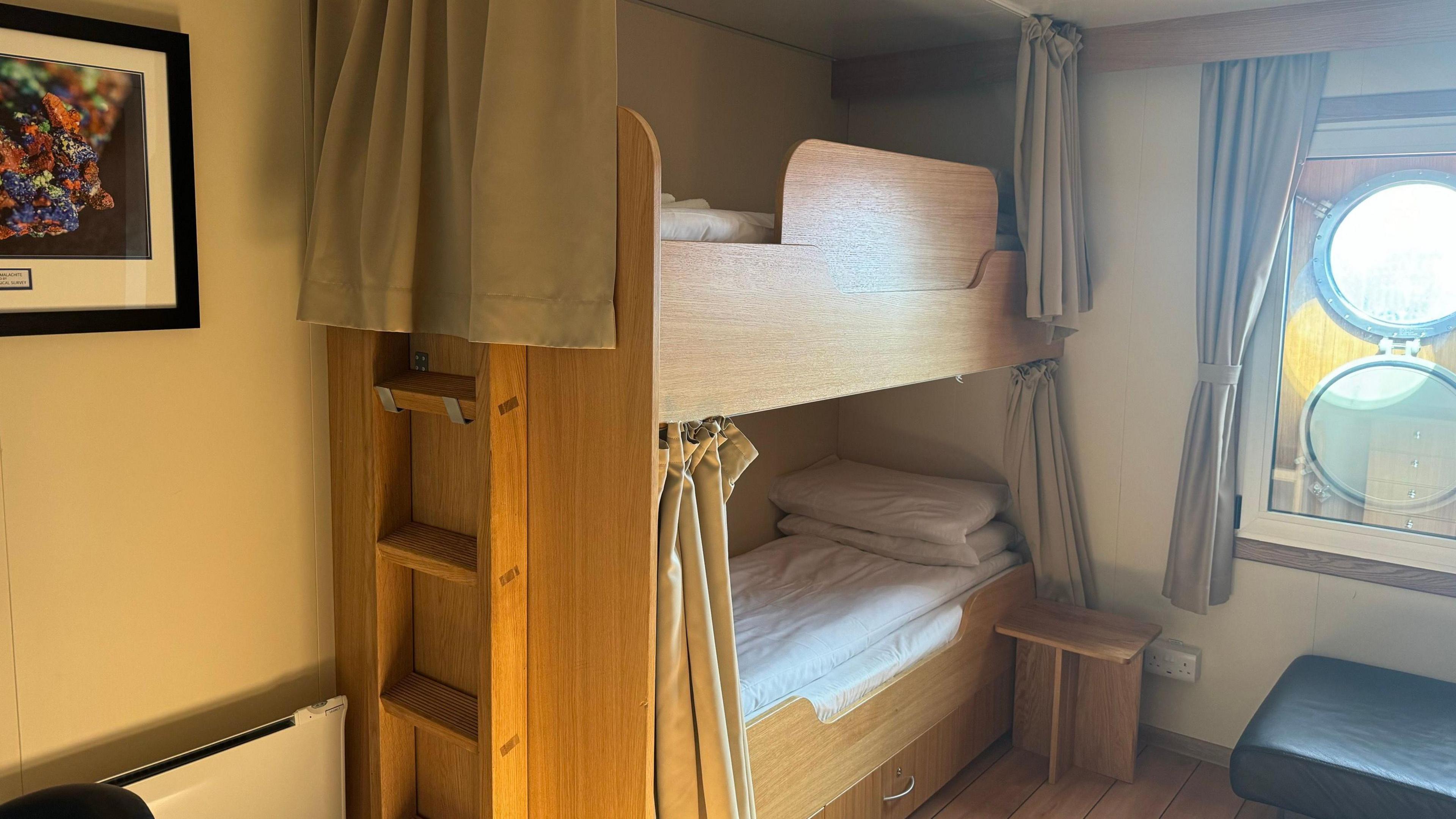 Wooden bunk beds in a cabin. There is a framed photo on the wall and two circular windows on another.