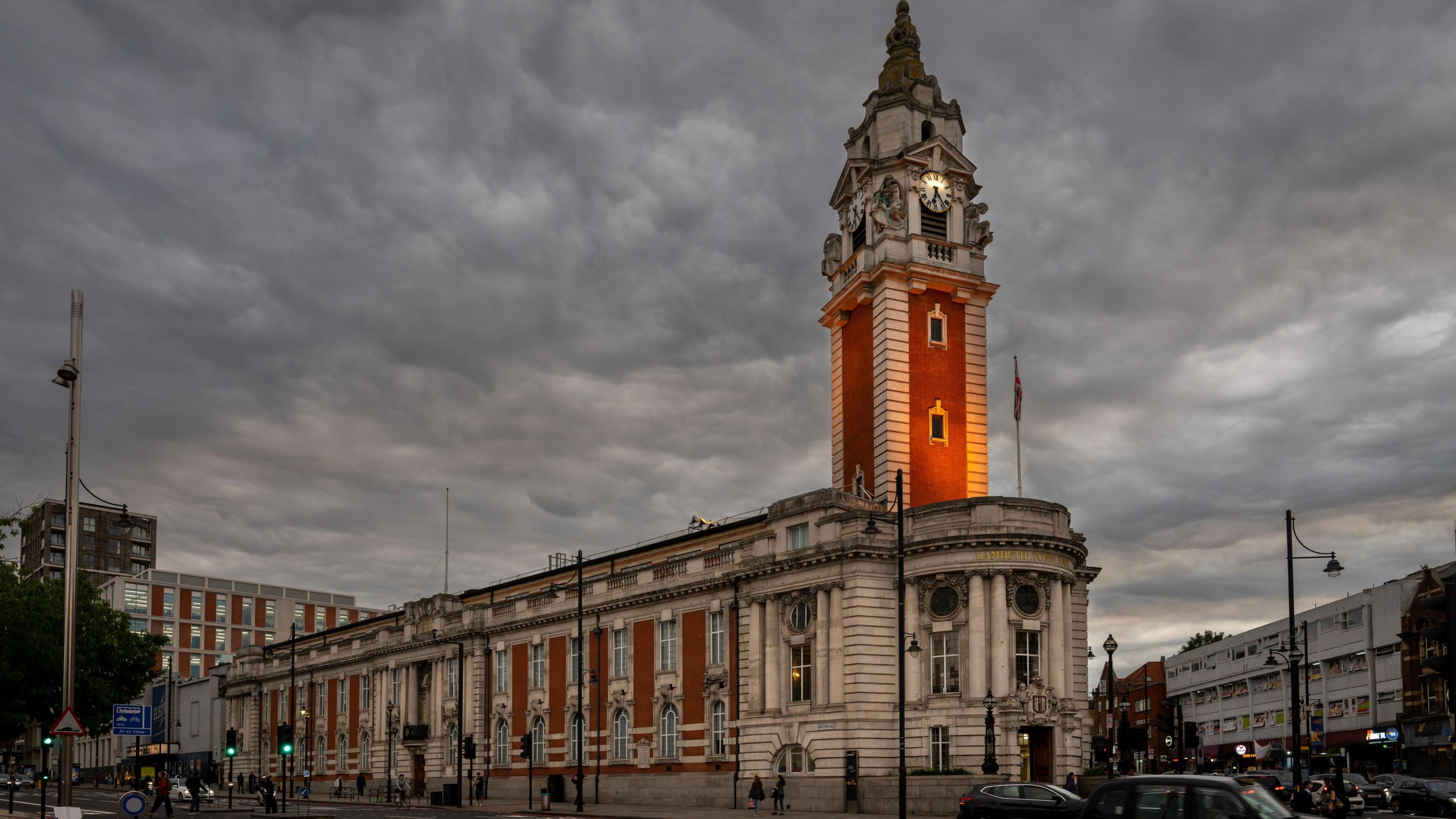 Lambeth Town Hall with its impressive clock tower in Brixton with dark grey clouds taking over the evening sky 