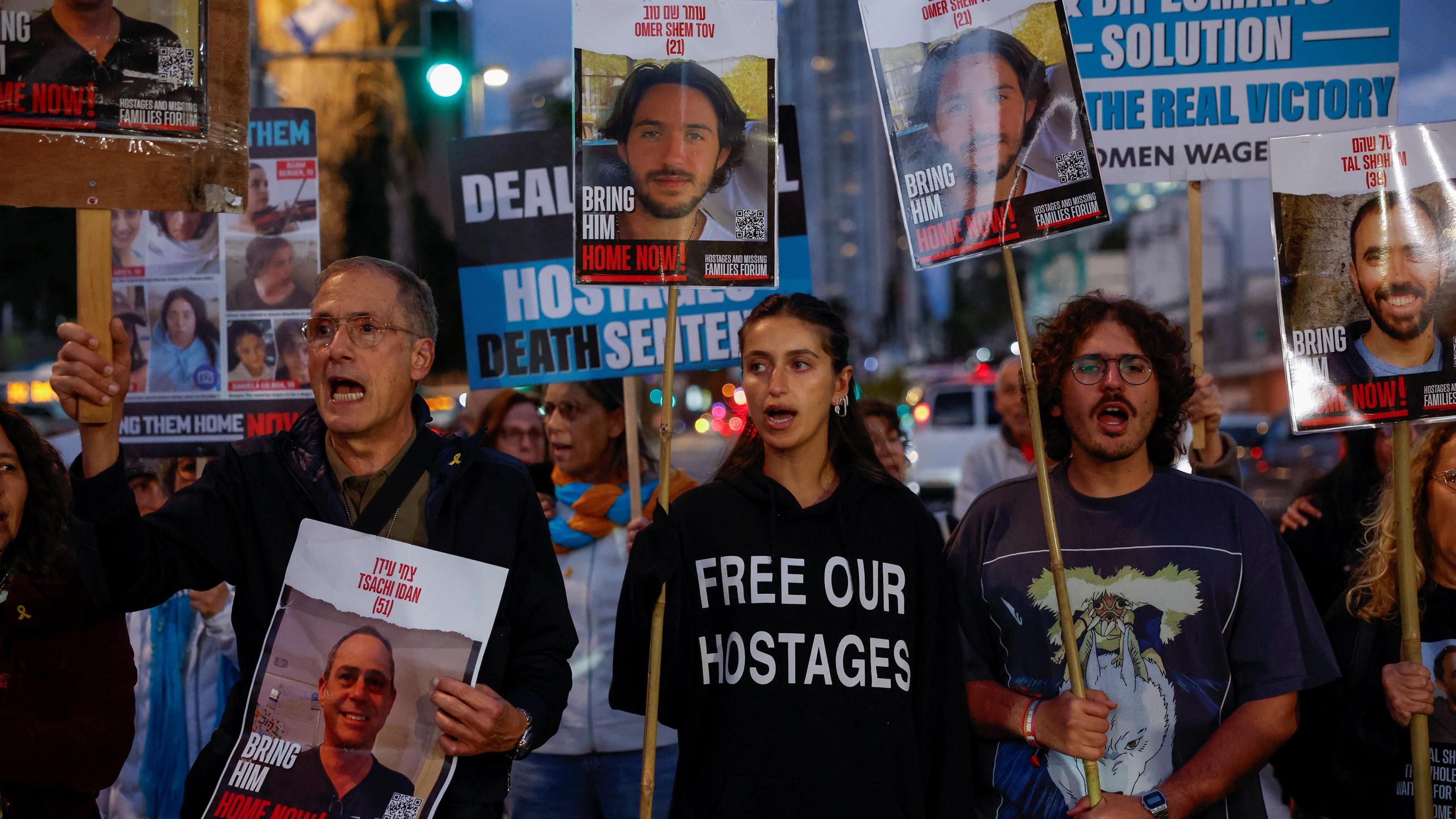 A crowd holds placards and posters calling for the return of hostages, including pictures of Omer Shem Tov.