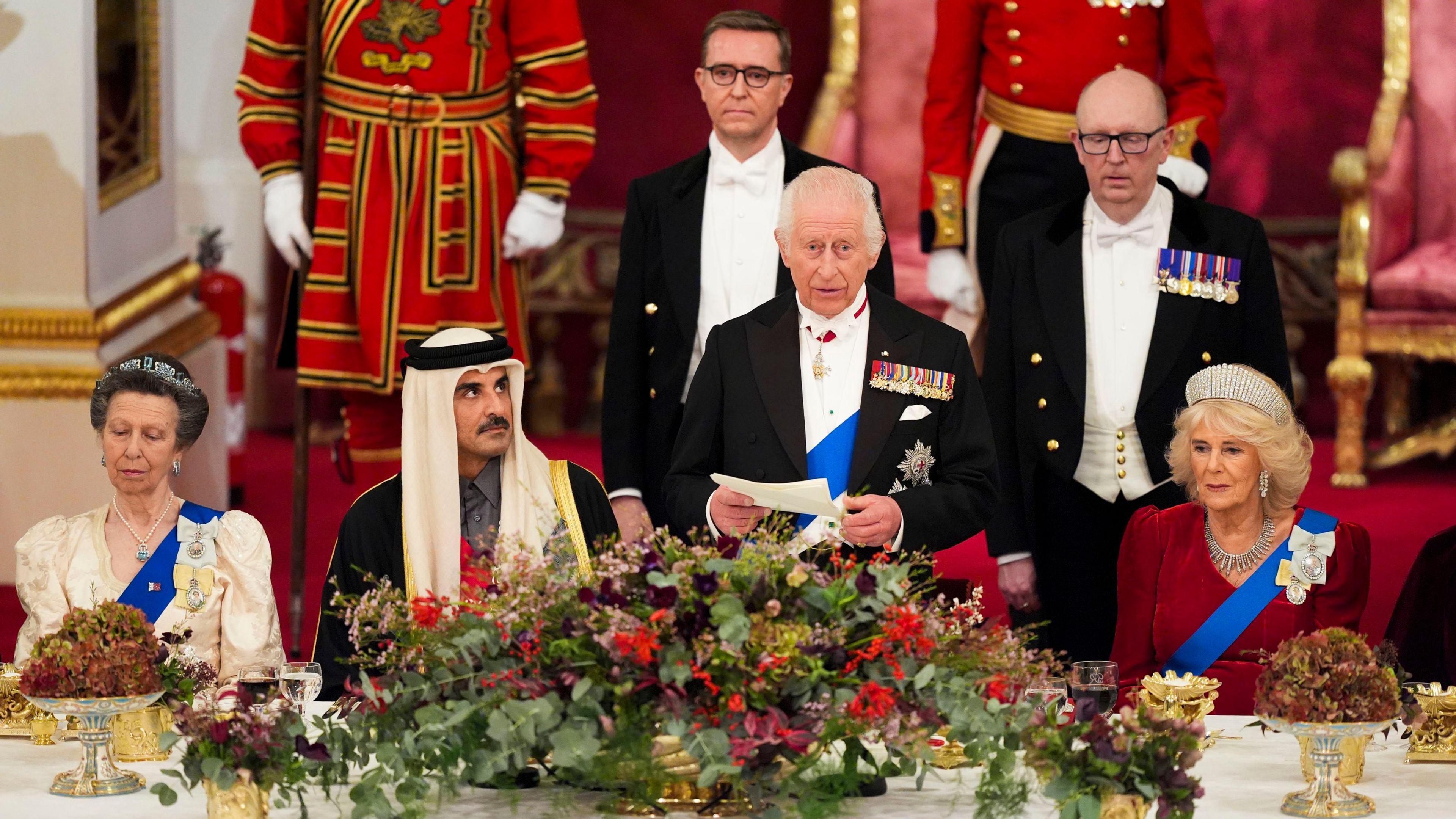 (left to right) Princess Anne, Sheikh Tamim, King Charles and Queen Anne sitting at the head table of the banquet. The King is standing, reading a speech from a piece of paper