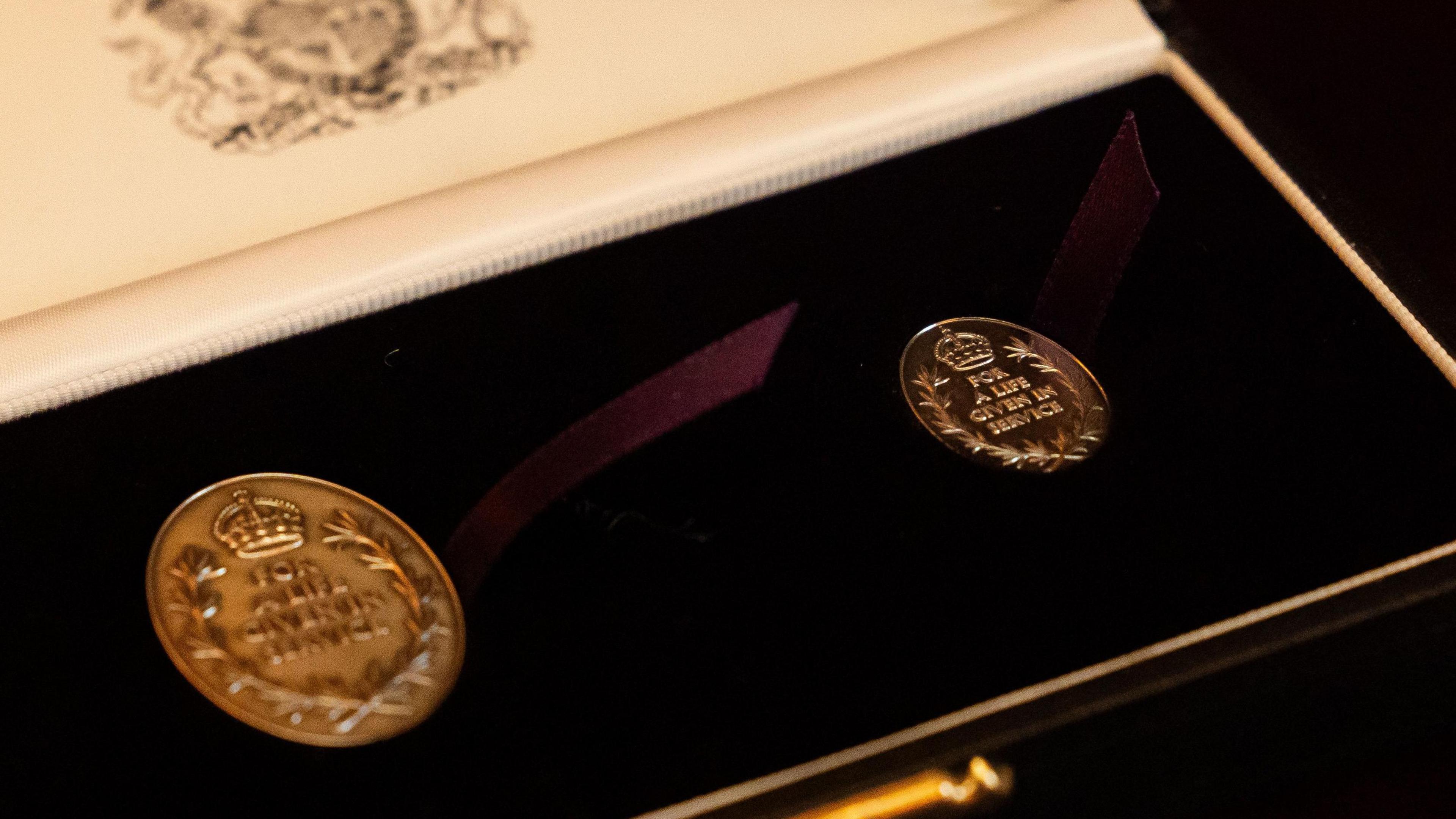 A presentation box holding two circular gold medals bearing the words "For a life given in service".