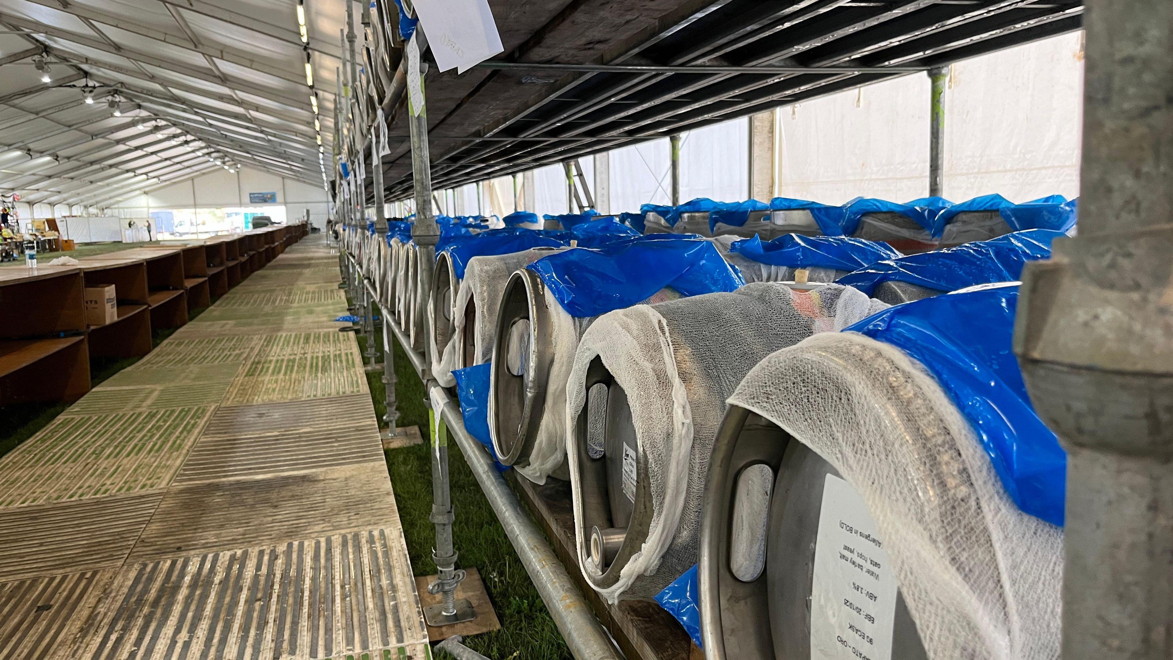Silver casks of beer placed in a row inside a white tent 