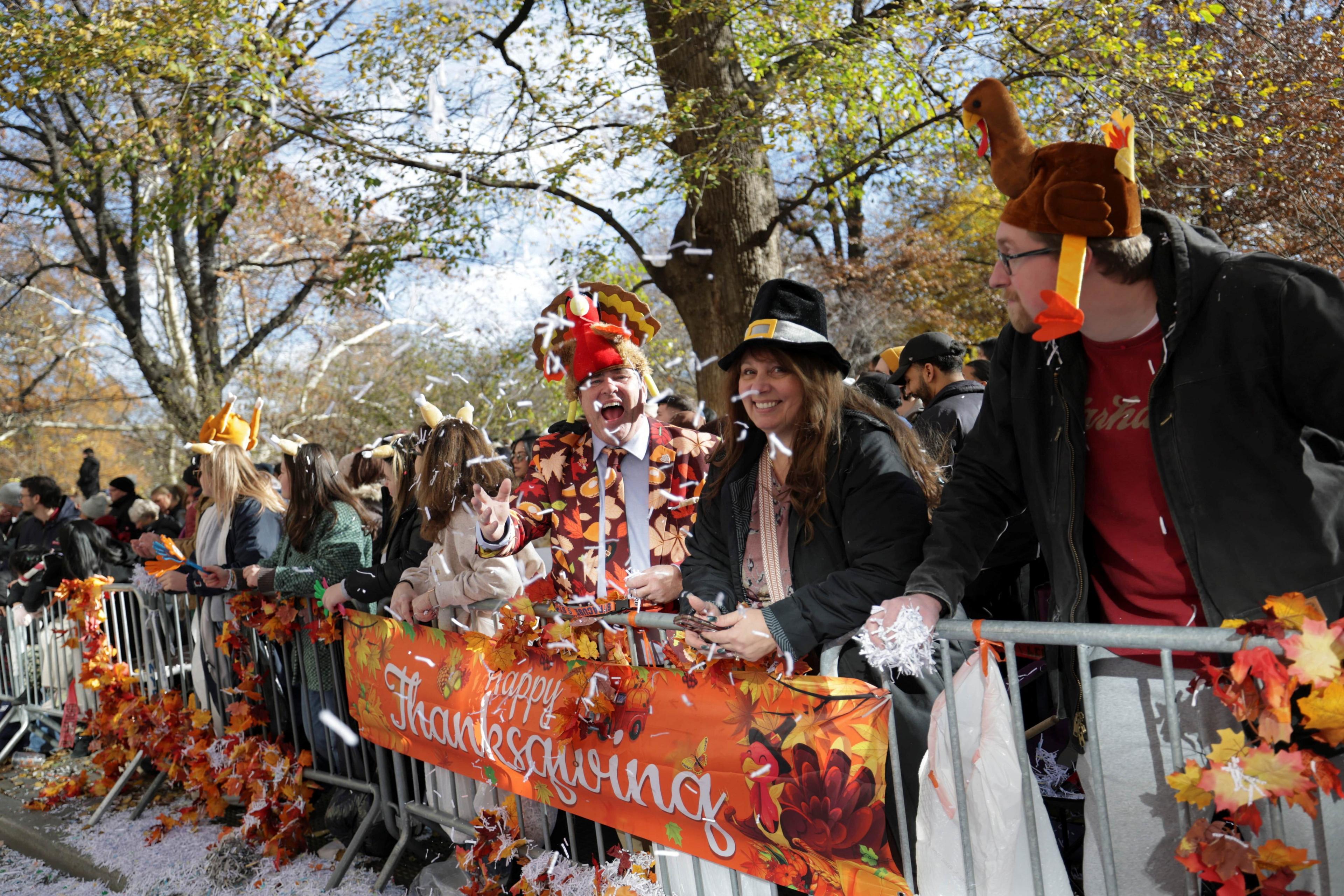 People stand at the barriers wearing turkey hats and throwing confetti.