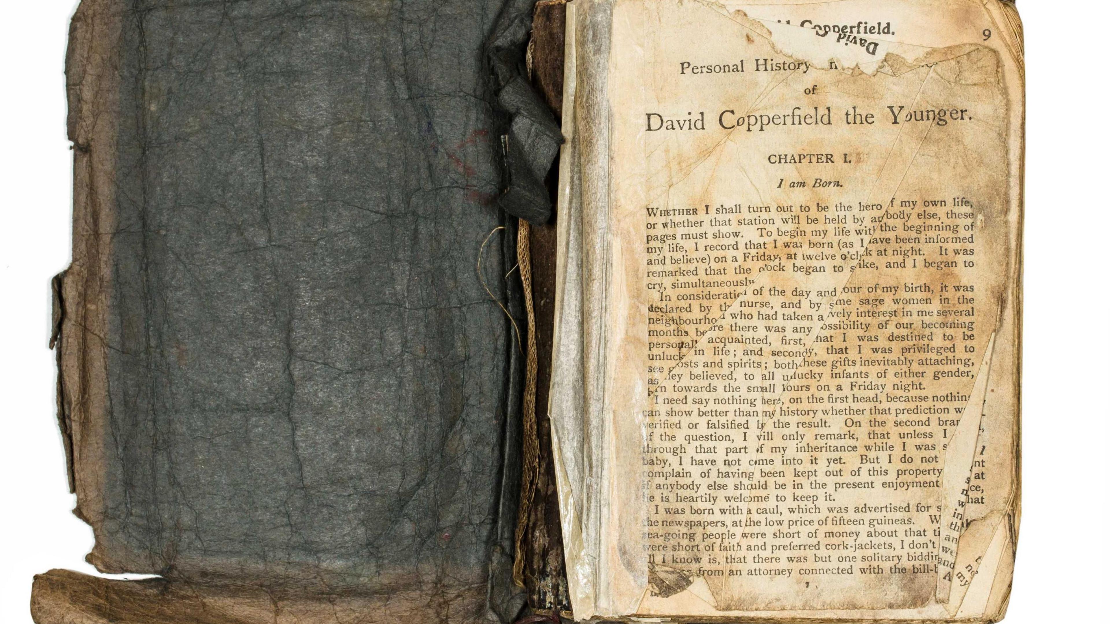 An old, damaged copy of David Copperfield opened at the first page. The book's dark brown jacket is cracked and stained with blubber. 