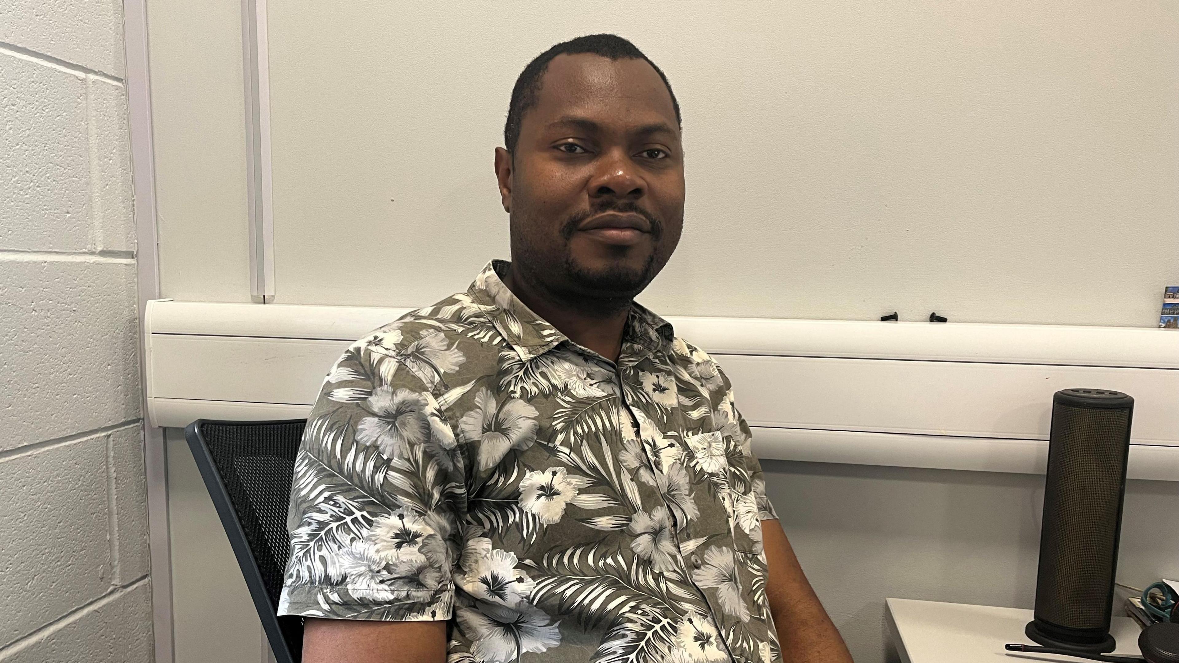 A man wearing a flowery shirt sat at a desk