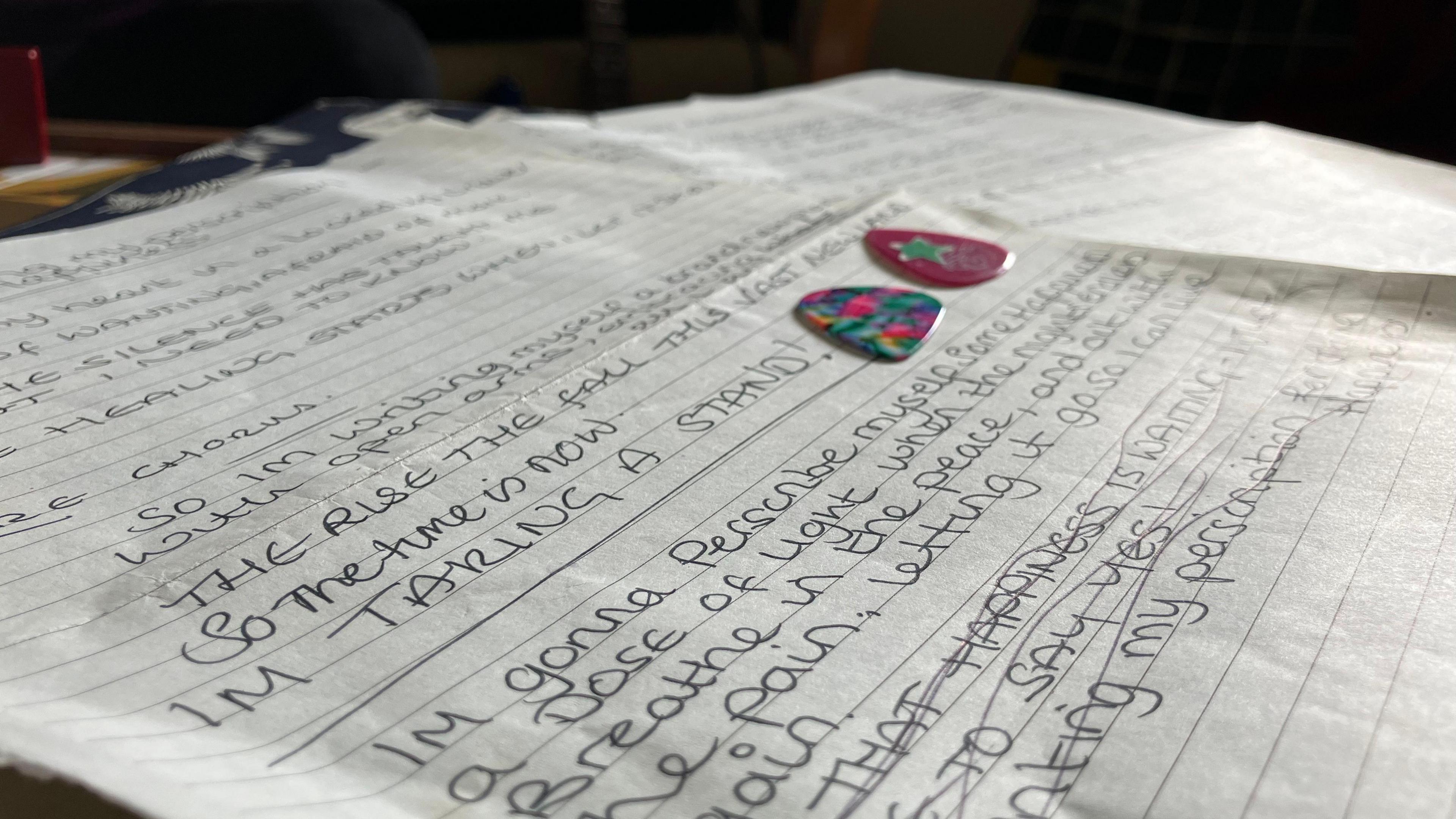 handwritten lines on a page, with two guitar plectrums