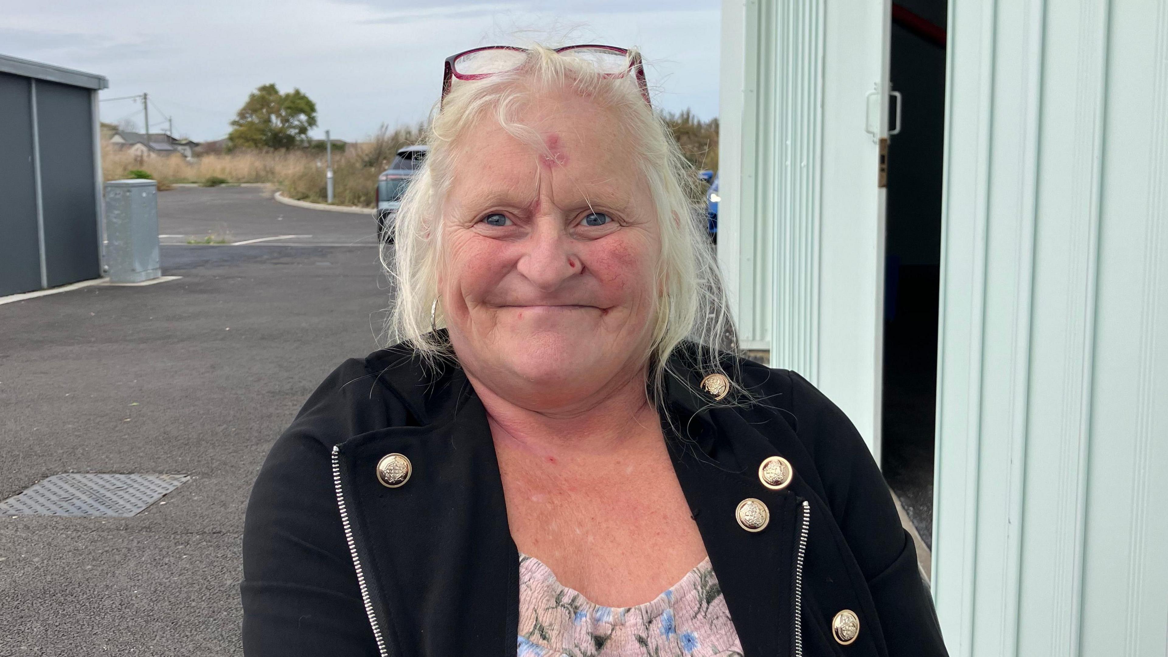 Jane smiling at the camera. She is wearing glasses on her head and a black jacket and a top.