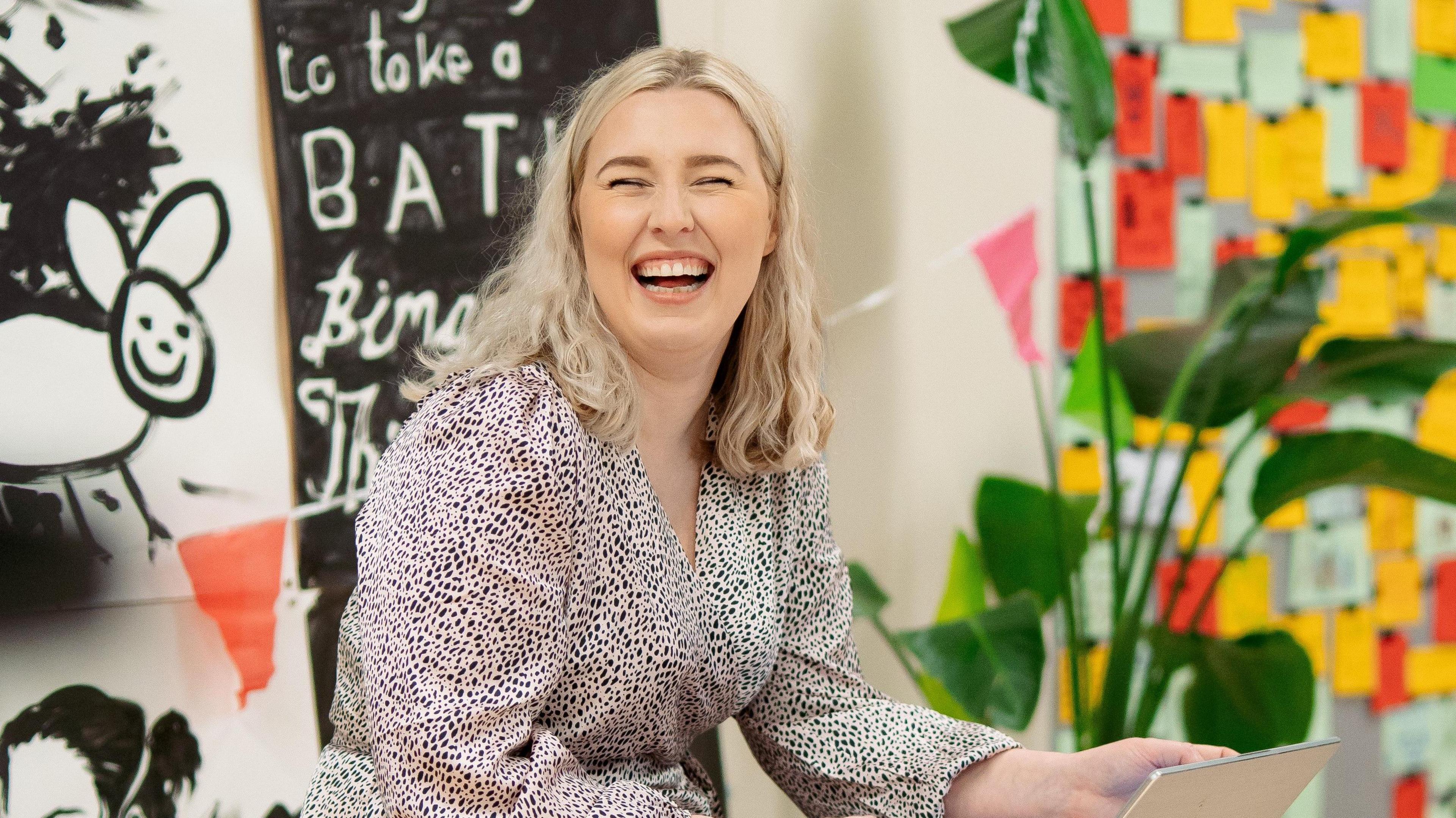 Sarah-Jane Montgomery, joint managing director of 2 Royal Avenue, smiling as she works at a pop-up event. She has long, blonde hair and is wearing a monochrome dress with puffed sleeves. 