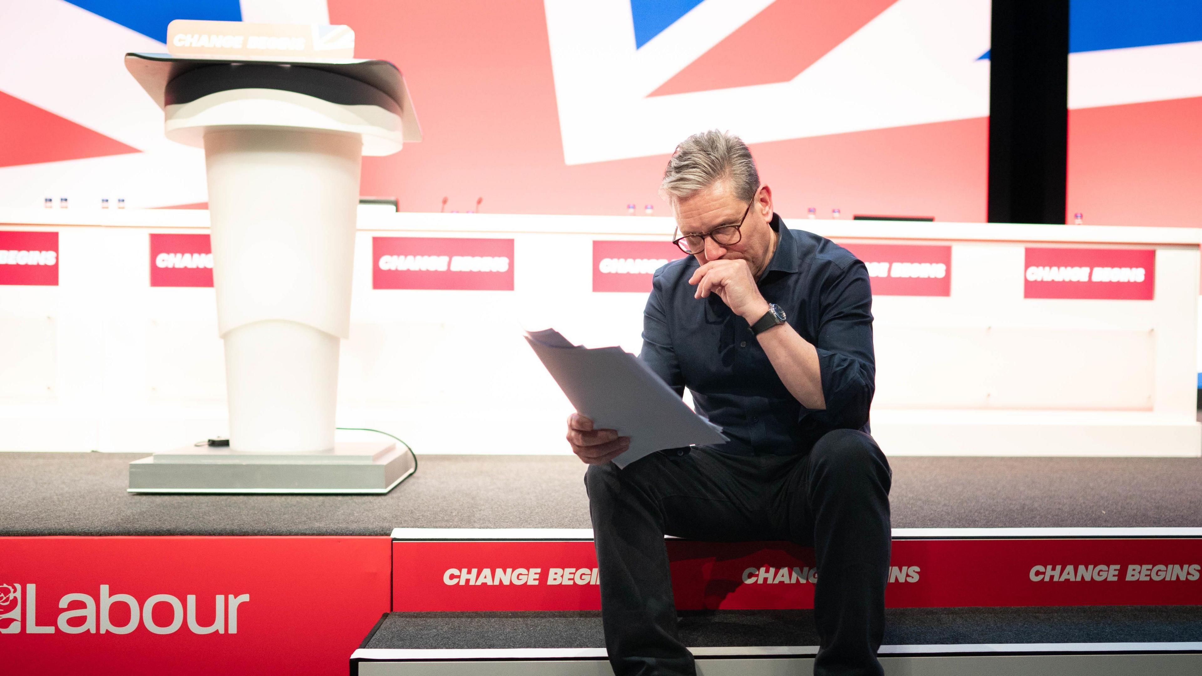 Keir Starmer studies his conference speech, sitting at the edge of the stage