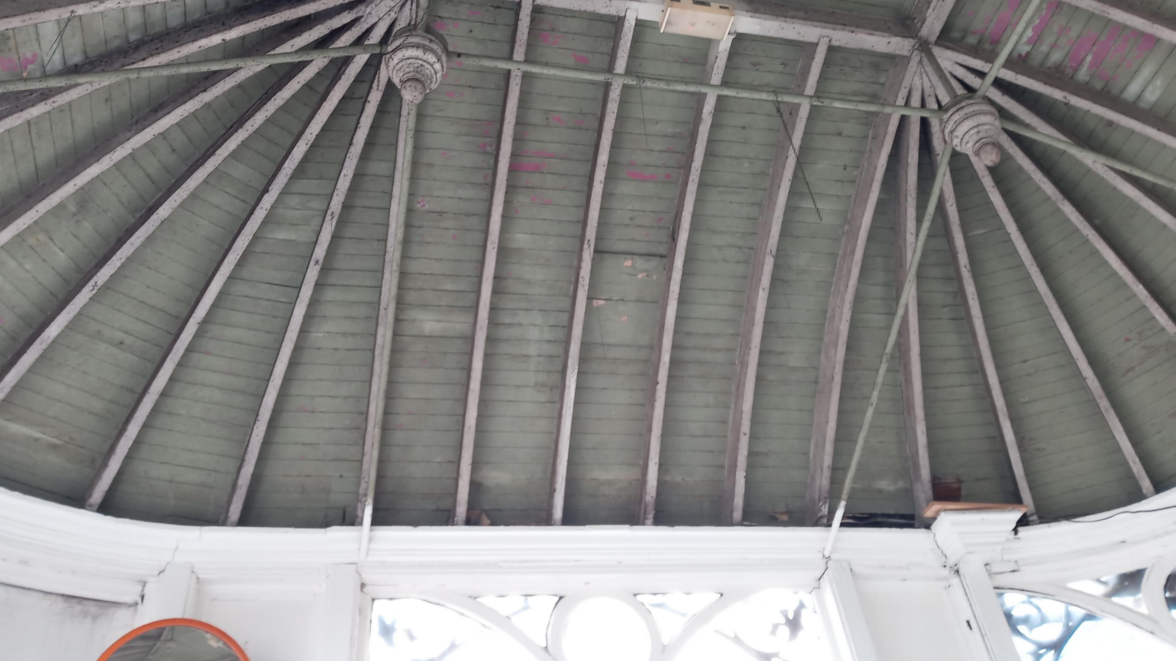 The interior of an intricate wooden roof, which has some paint flaking off. 