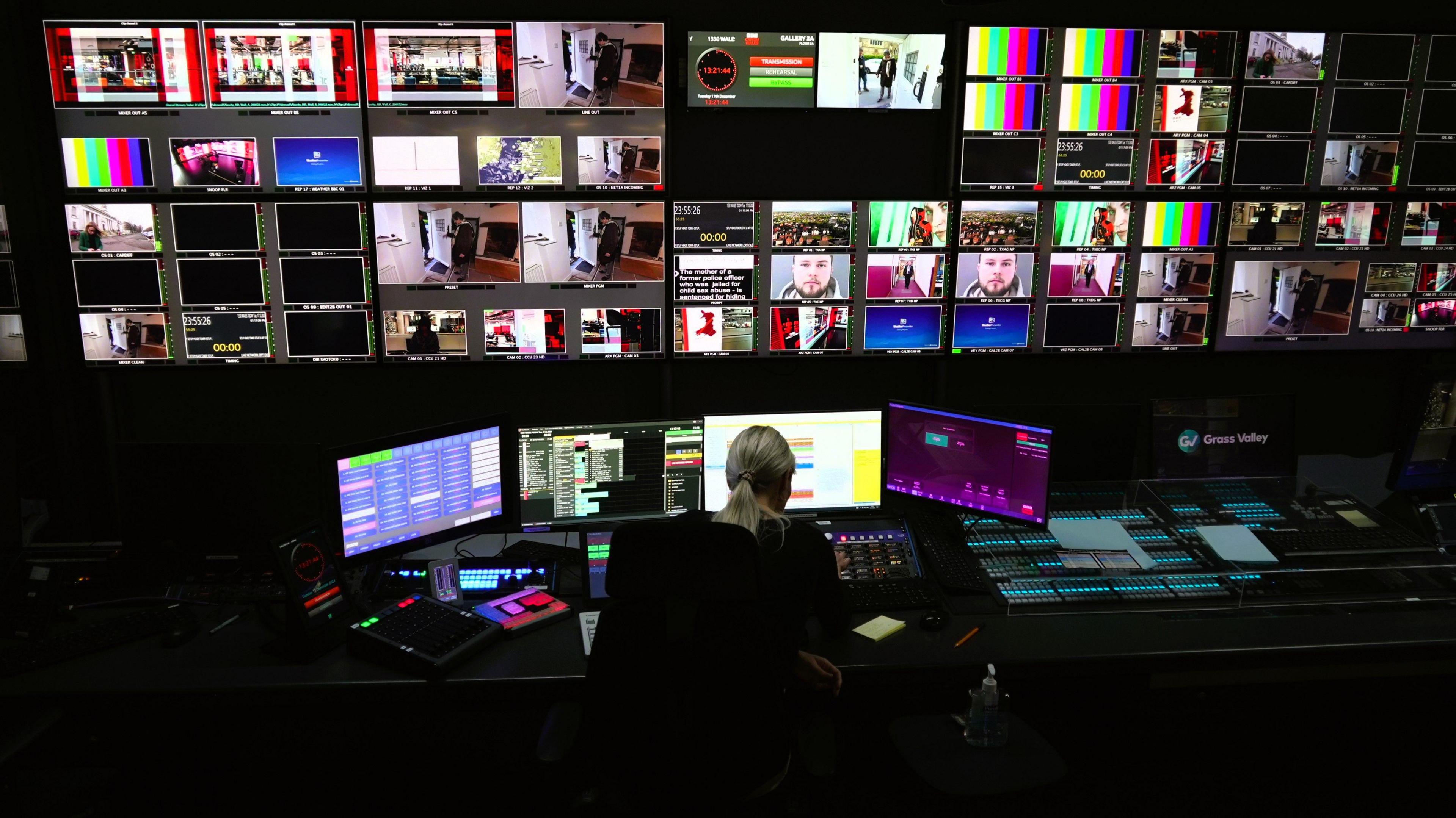 A female director sits in front of a bank of screens inside a studio gallery at BBC Cymru Wales headquarters in Cardiff