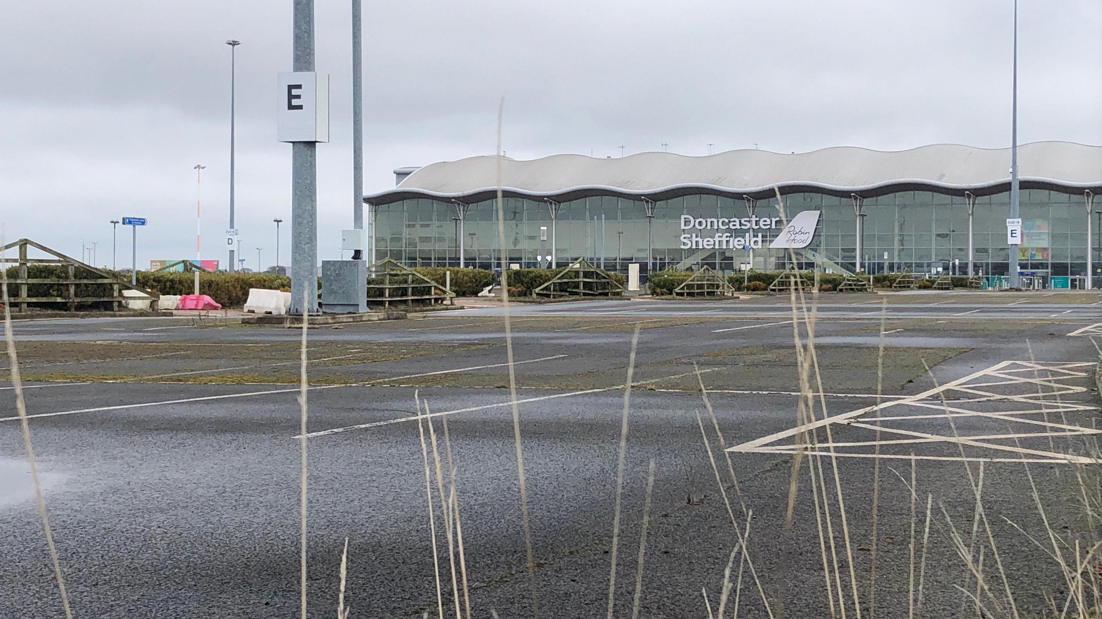 An empty car park in front of a big glass building. A huge sign that reads "Doncaster Sheffield Robin Hood" sits at its centre. The site looks empty and disused.
