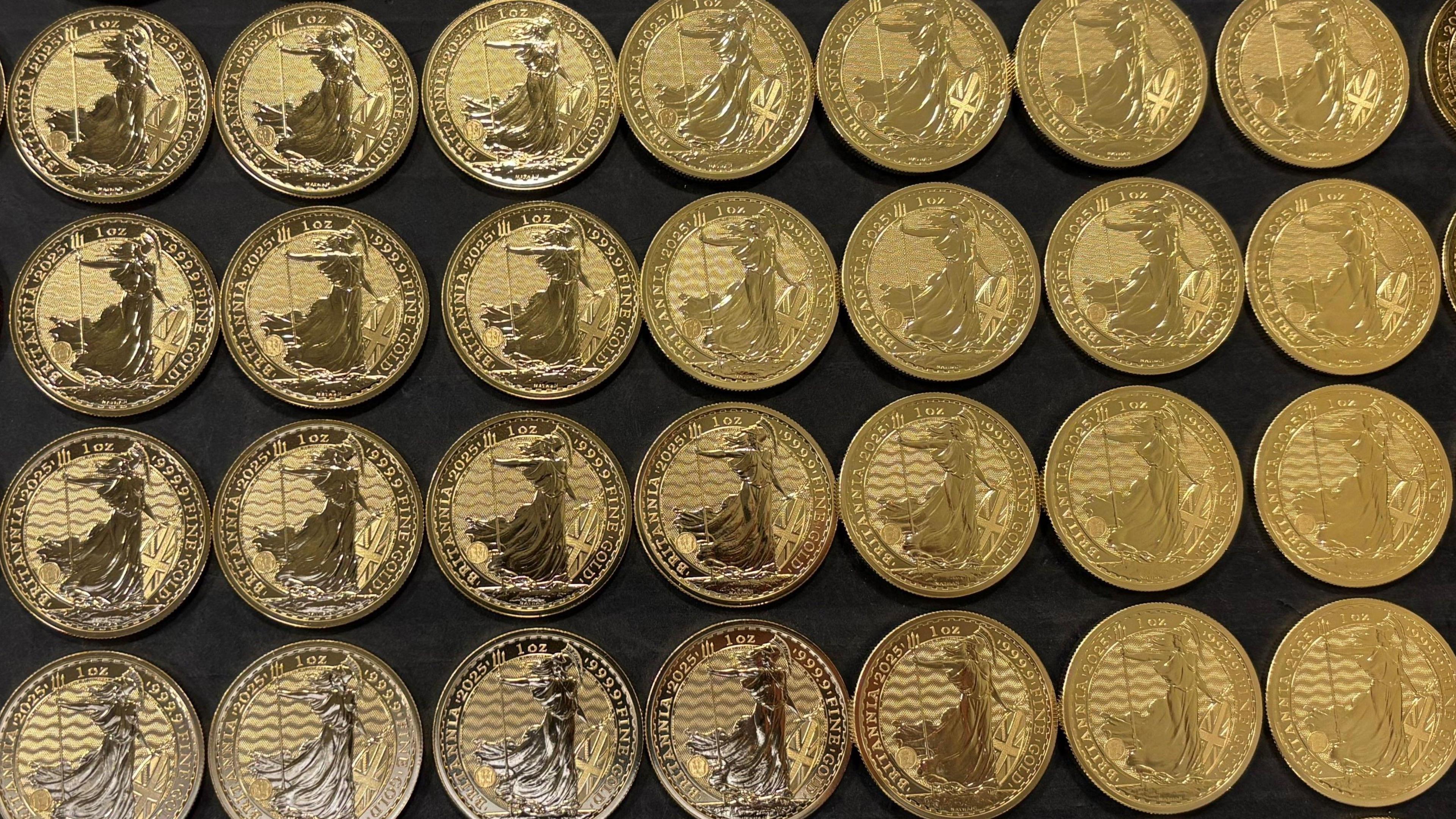 A tray of 24 carat gold bullion coins bearing the image of Britannia laid out side by side.