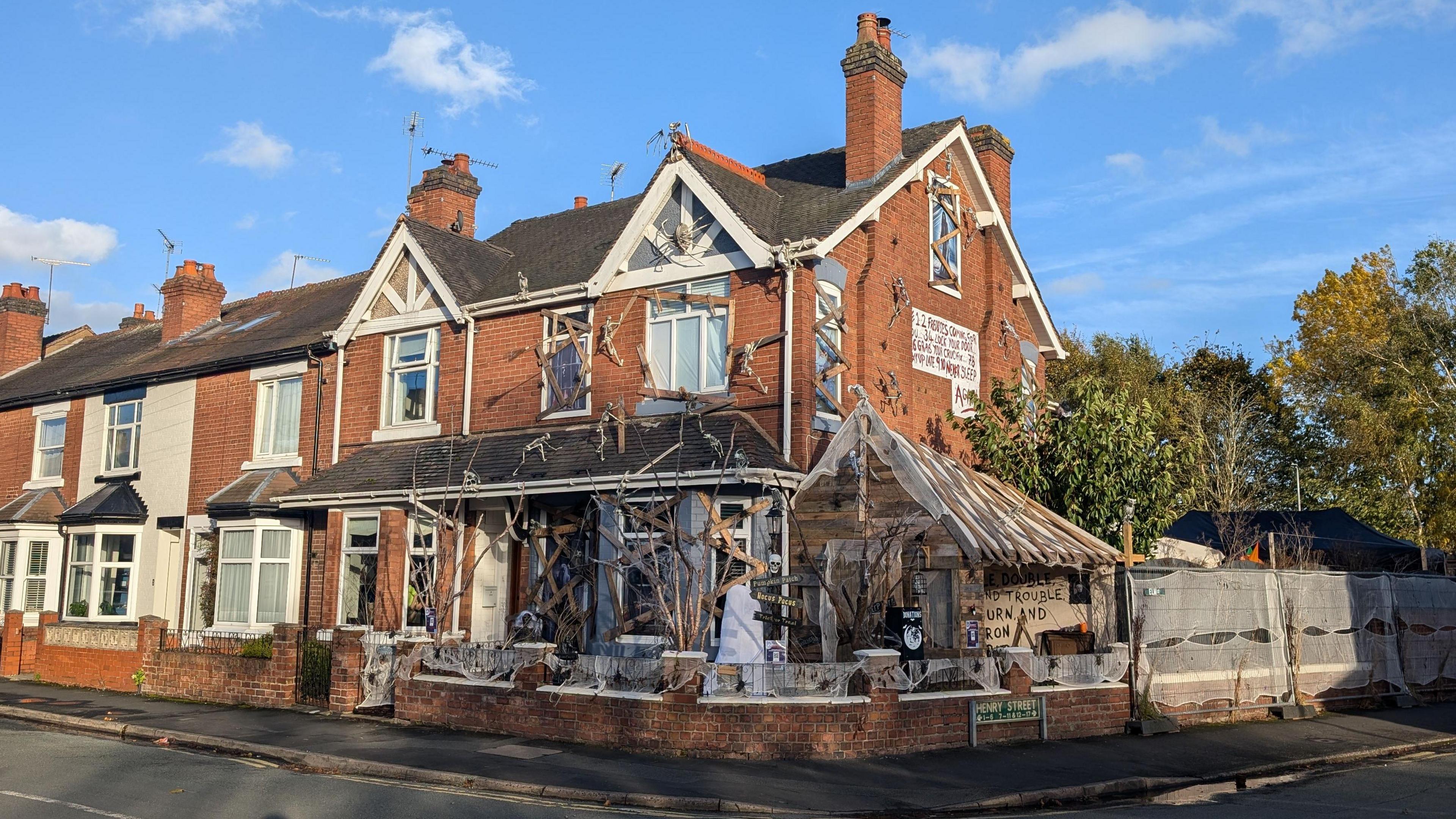 A semi-detached house at the end of the street covered in Halloween decorations. Boards have been placed across windows and doors while skeletons can be seen climbing the walls.