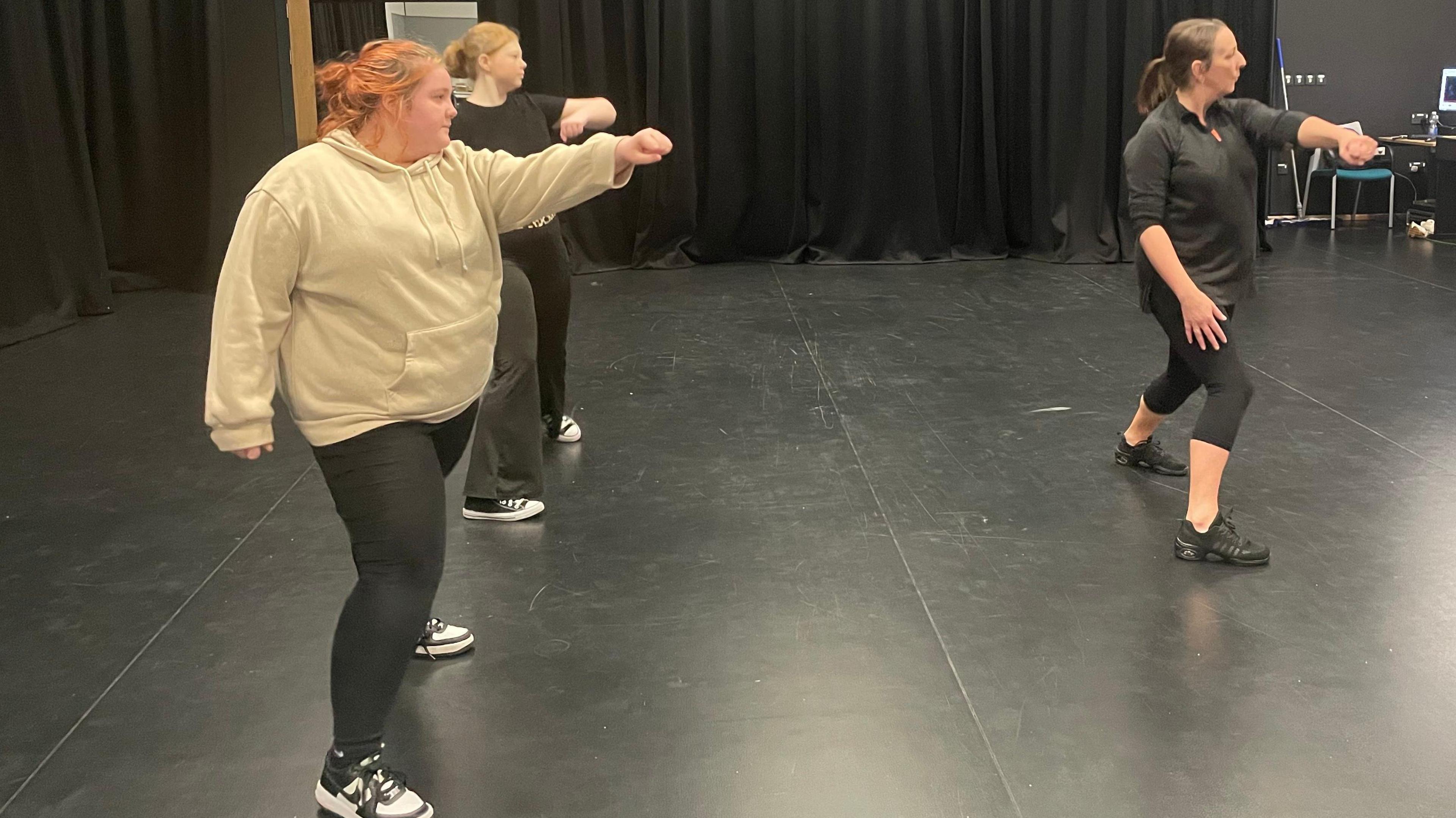 Two students and a teacher in the middle of practising a dance routine in a dance studio