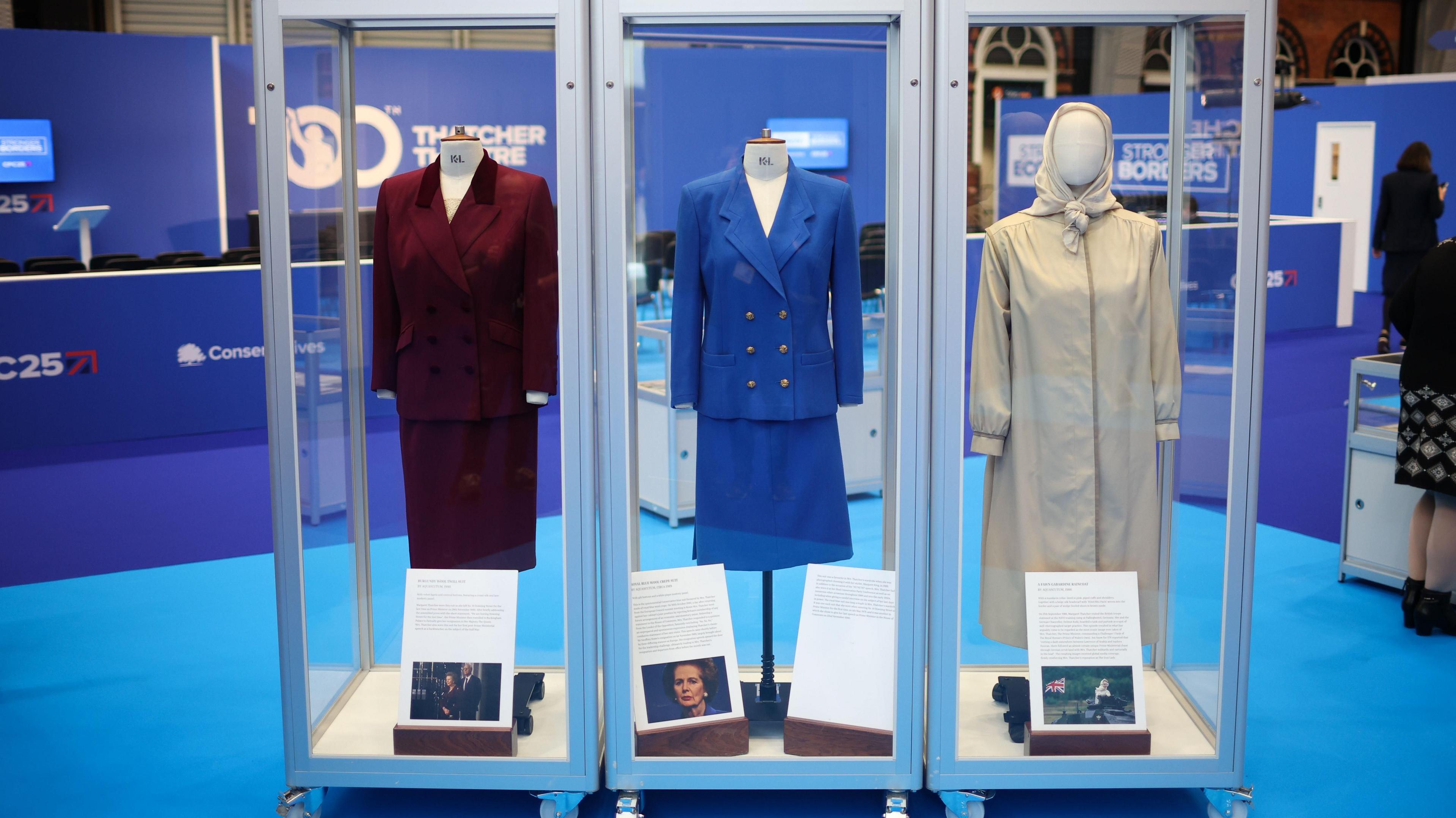 Three display cabinets at Conservative party conference holding outfits worn by Margaret Thatcher.