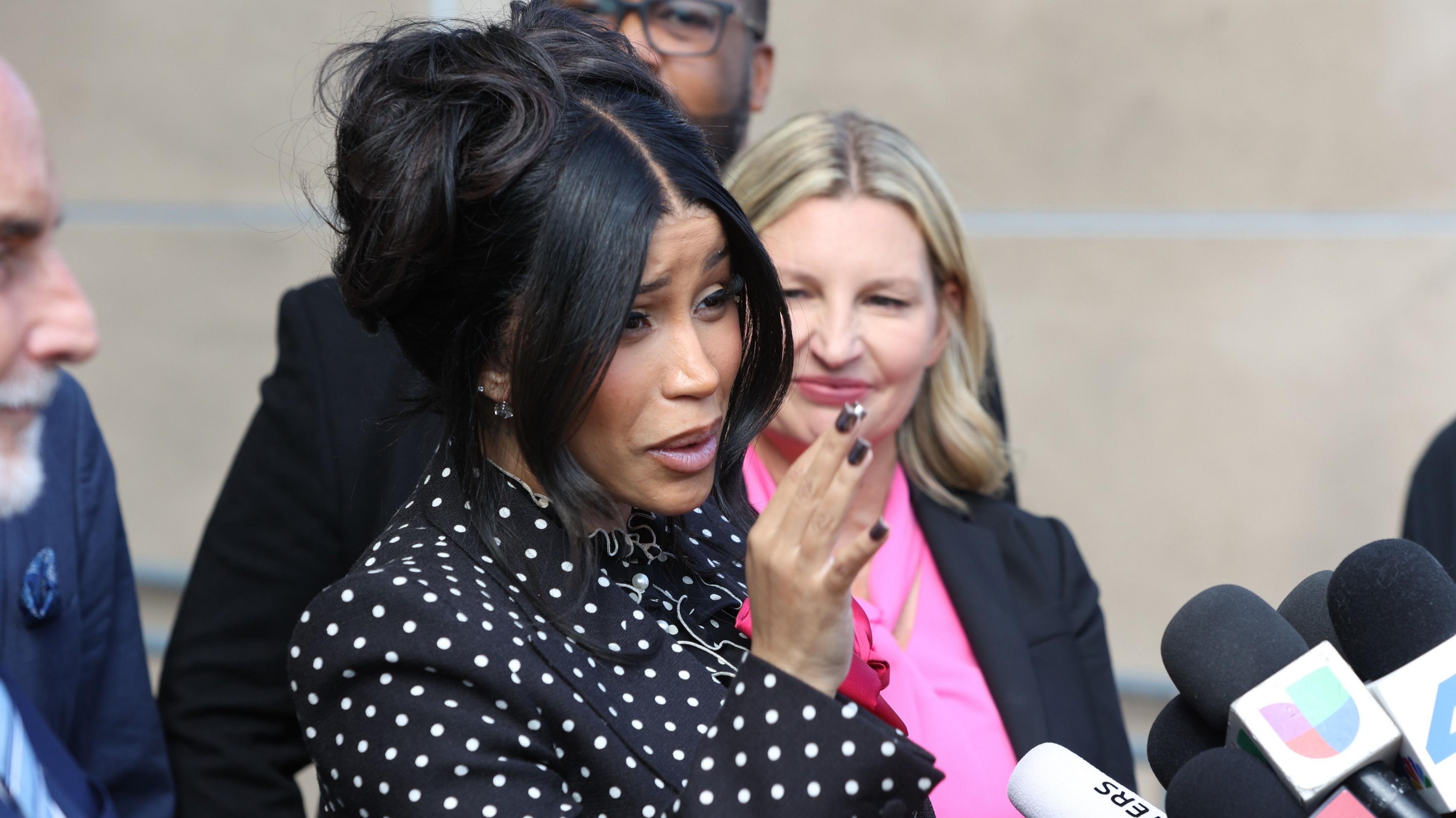 Cardi B speaks to reporters outside court. She has black hair tied up and wears a black top with white polka dots