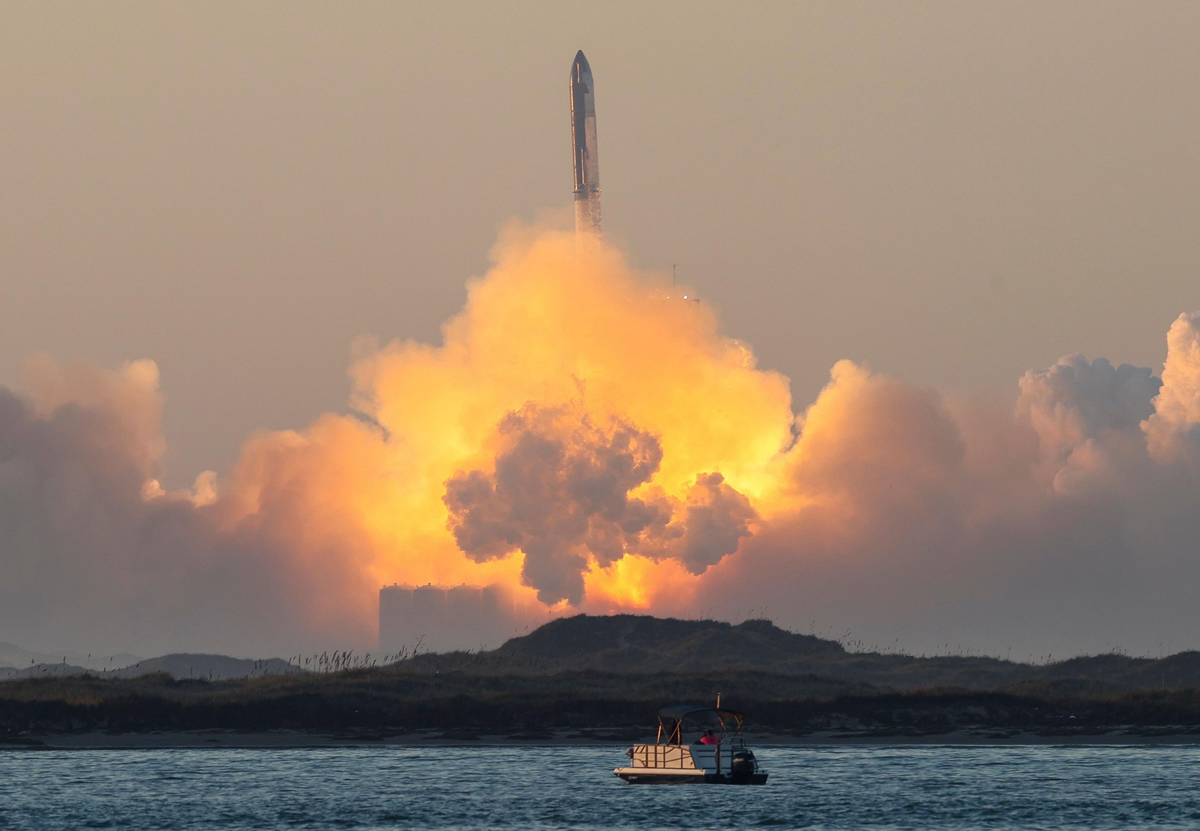 A rocket launch along the coast, with a boat on the water in the foreground