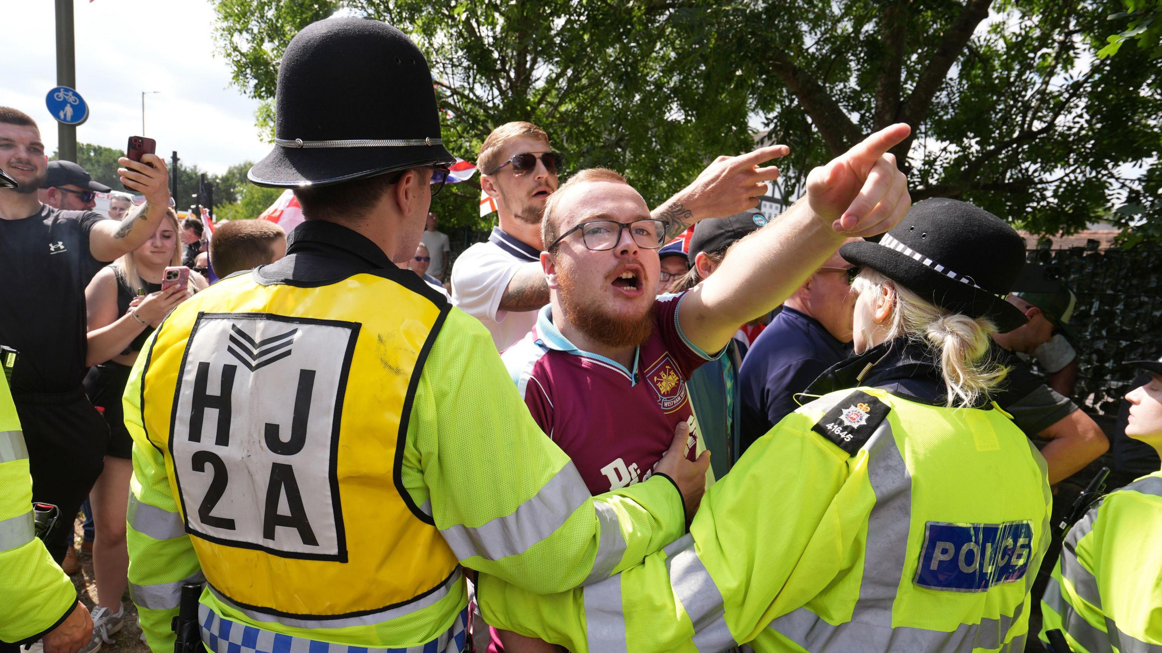 A man at a protest is held back by police.