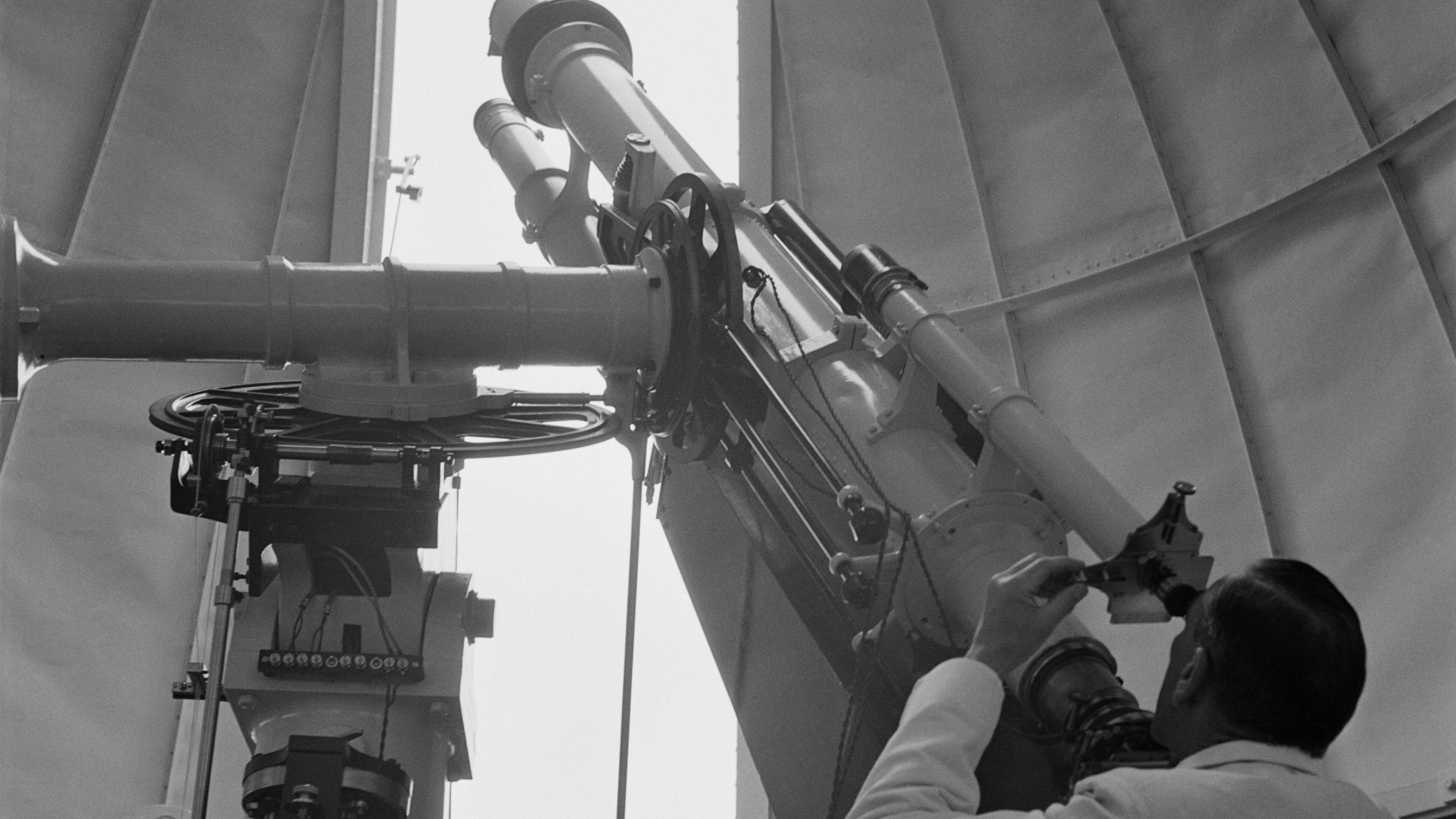 Senior experimental officer HHJ Barton using a photoheliograph attached to the refractor to take an exposure of the sun, through the roof of the dome in the solar building at the Royal Observatory, in the grounds of Herstmonceux Castle, near Herstmonceux, East Sussex, England, 1949.